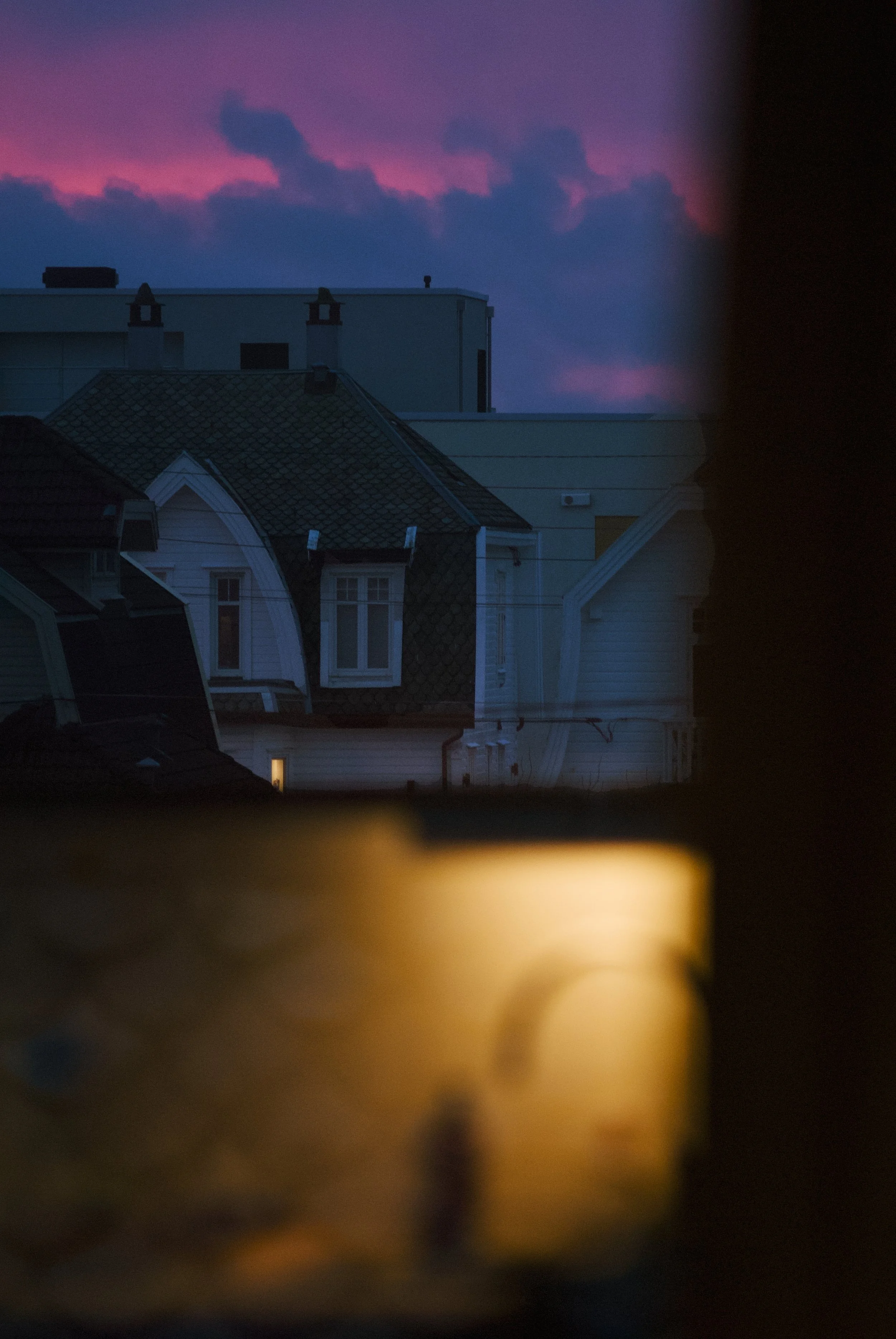 View of rooftops and a building against a dusk sky with pink and purple clouds, partially obscured by a dark frame.