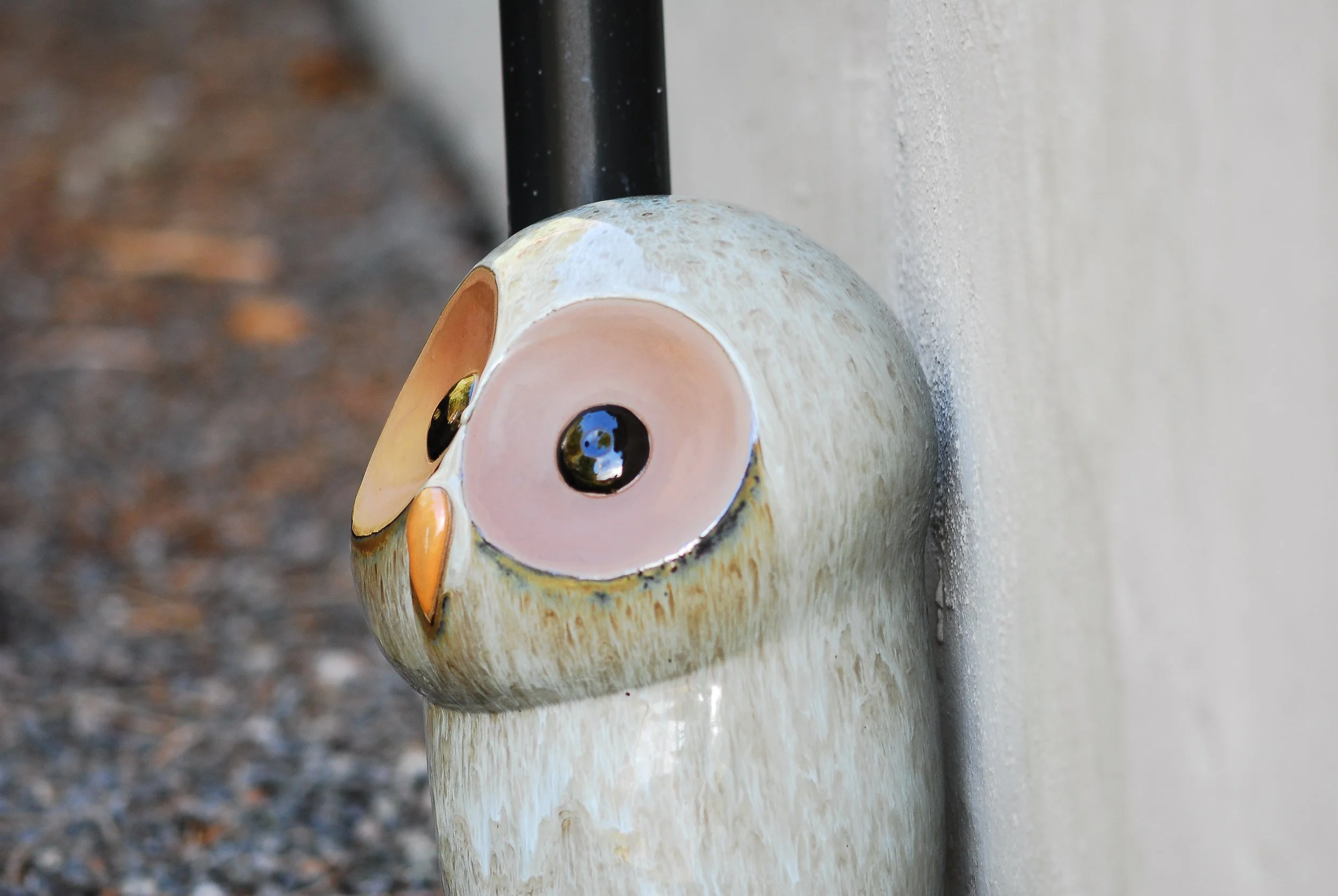 Decorative owl sculpture with large eyes, perched on a surface and leaning against a wall.