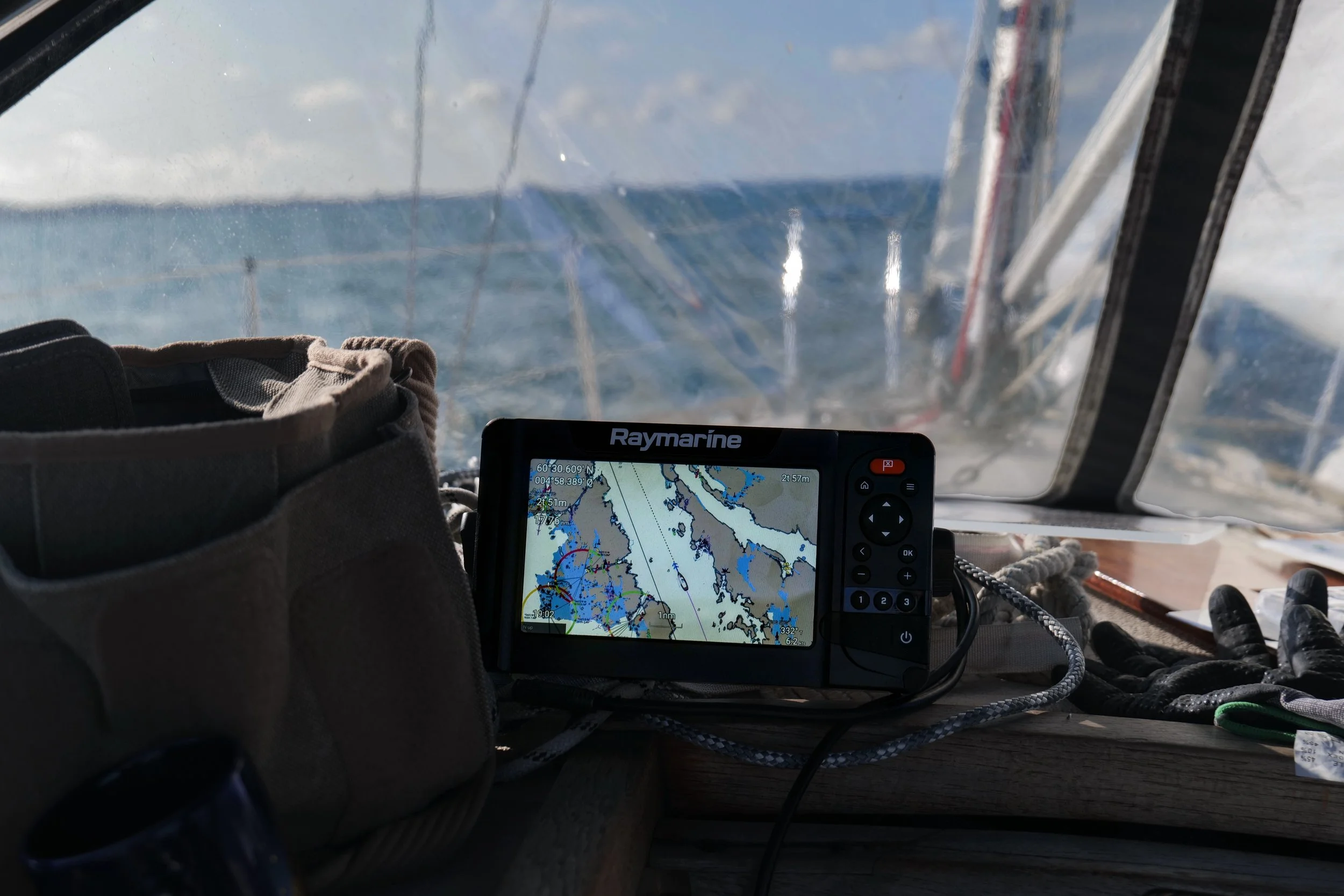 A GPS navigation device on a boat displaying a nautical chart, with fishing gloves and a bag nearby, and water visible through the window in the background.