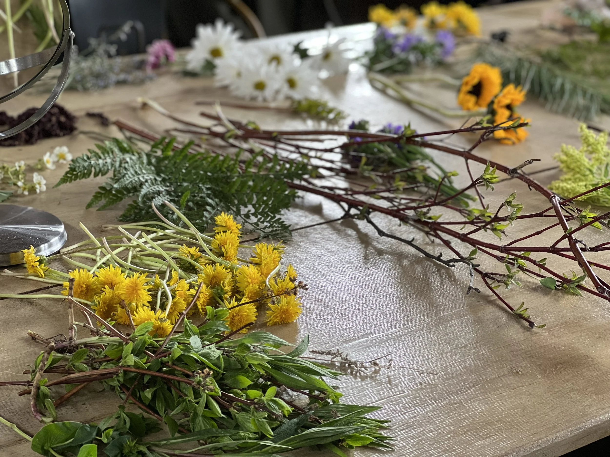 Various flowers, leaves, and branches arranged on a wooden table.