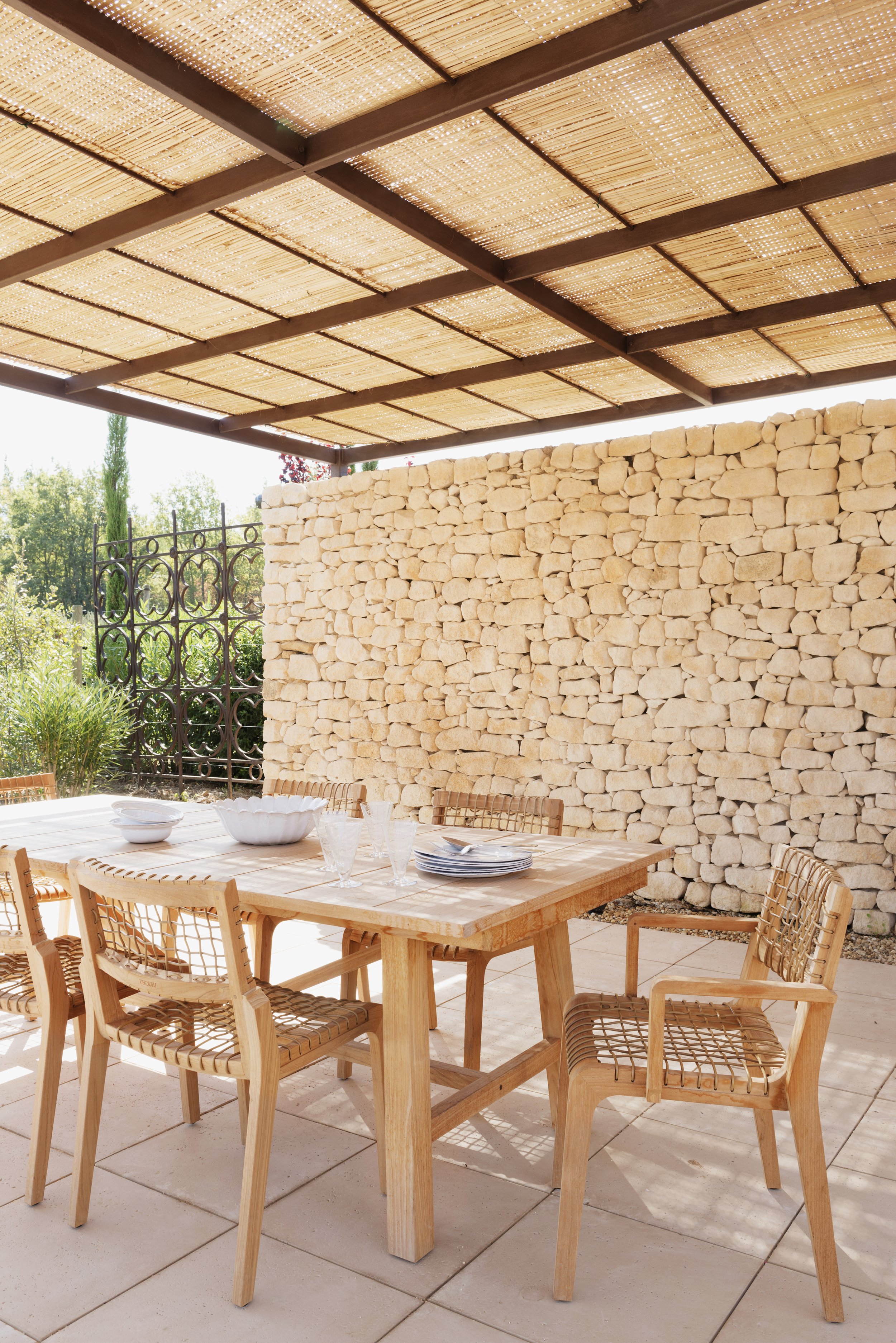 Detail of the outdoor dining table located in front of a dry stone wall, beneath a shade structure.