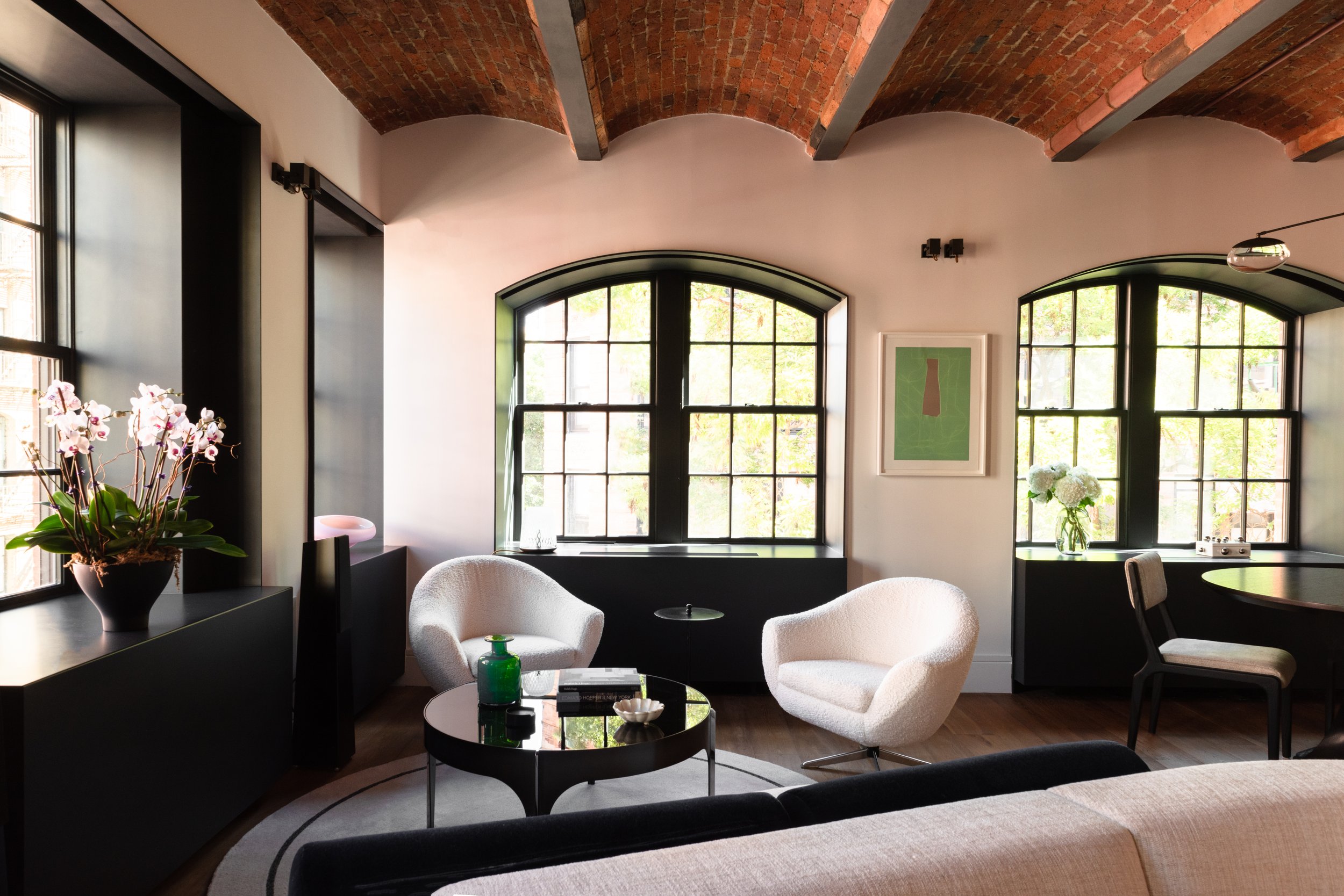 Wide interior photo of the relaxed sitting area in front of the large arched windows, beneath the exposed brick ceiling vaults. 