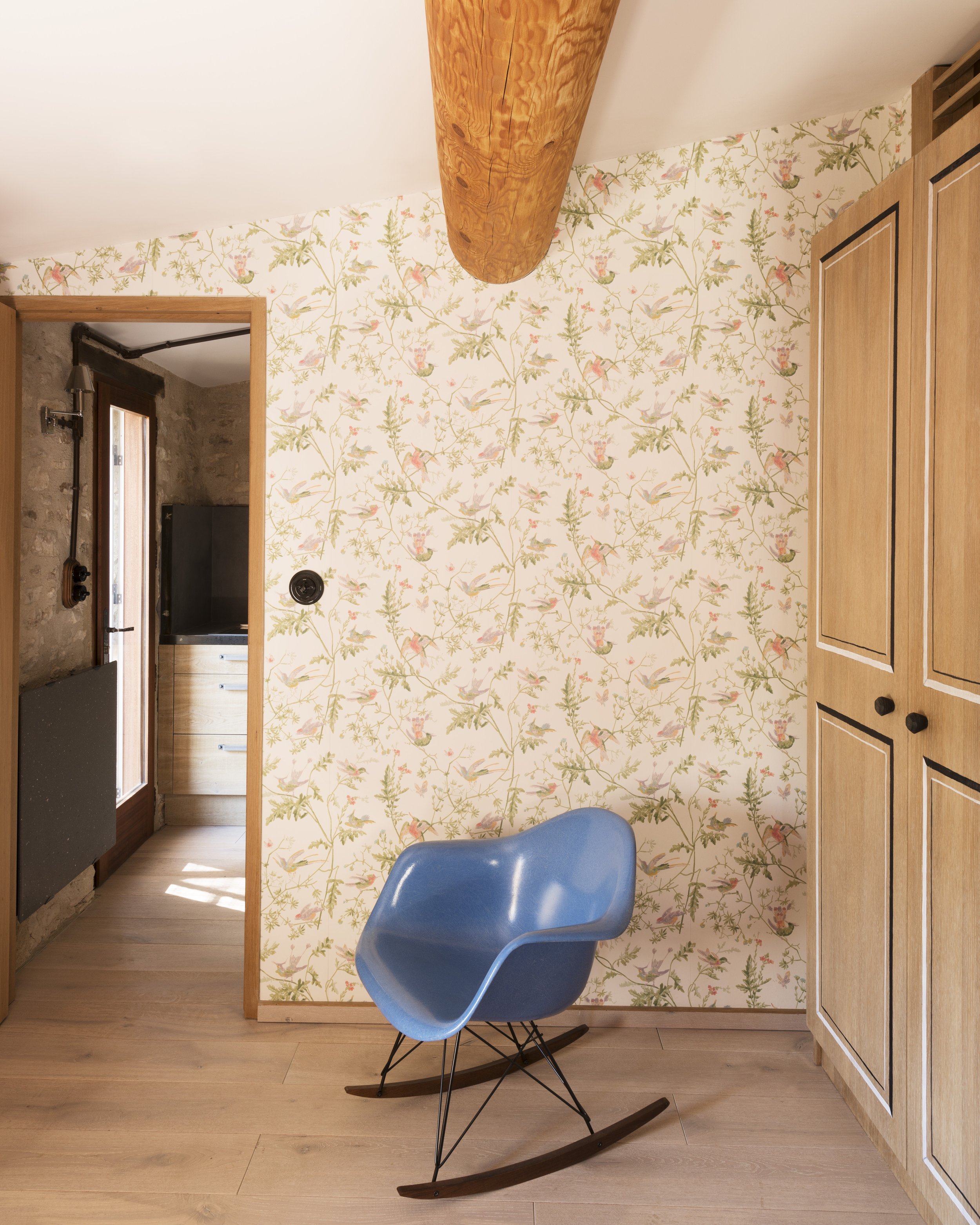 Detail of one of the bedrooms with a playful hummingbird and botanical wallpaper with a pale blue Eames molded rocking chair in front of the wardrobe.