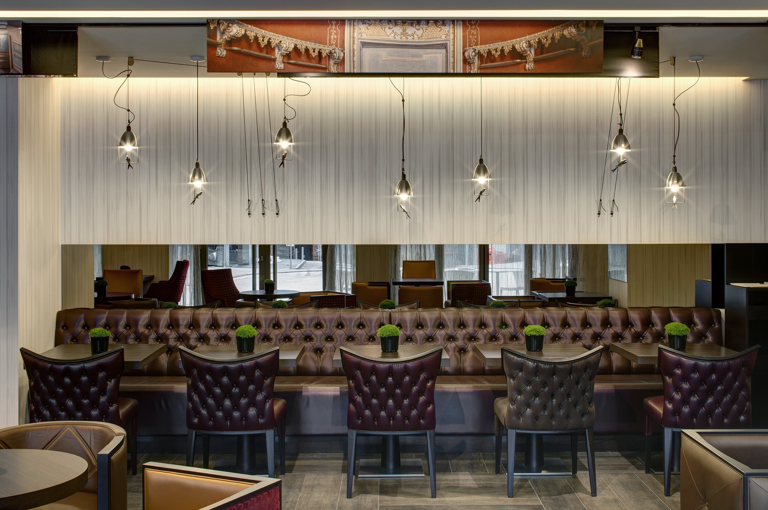 Detail of banquette seating in the restaurant with the cast iron bird hanging lights suspended at varying heights.