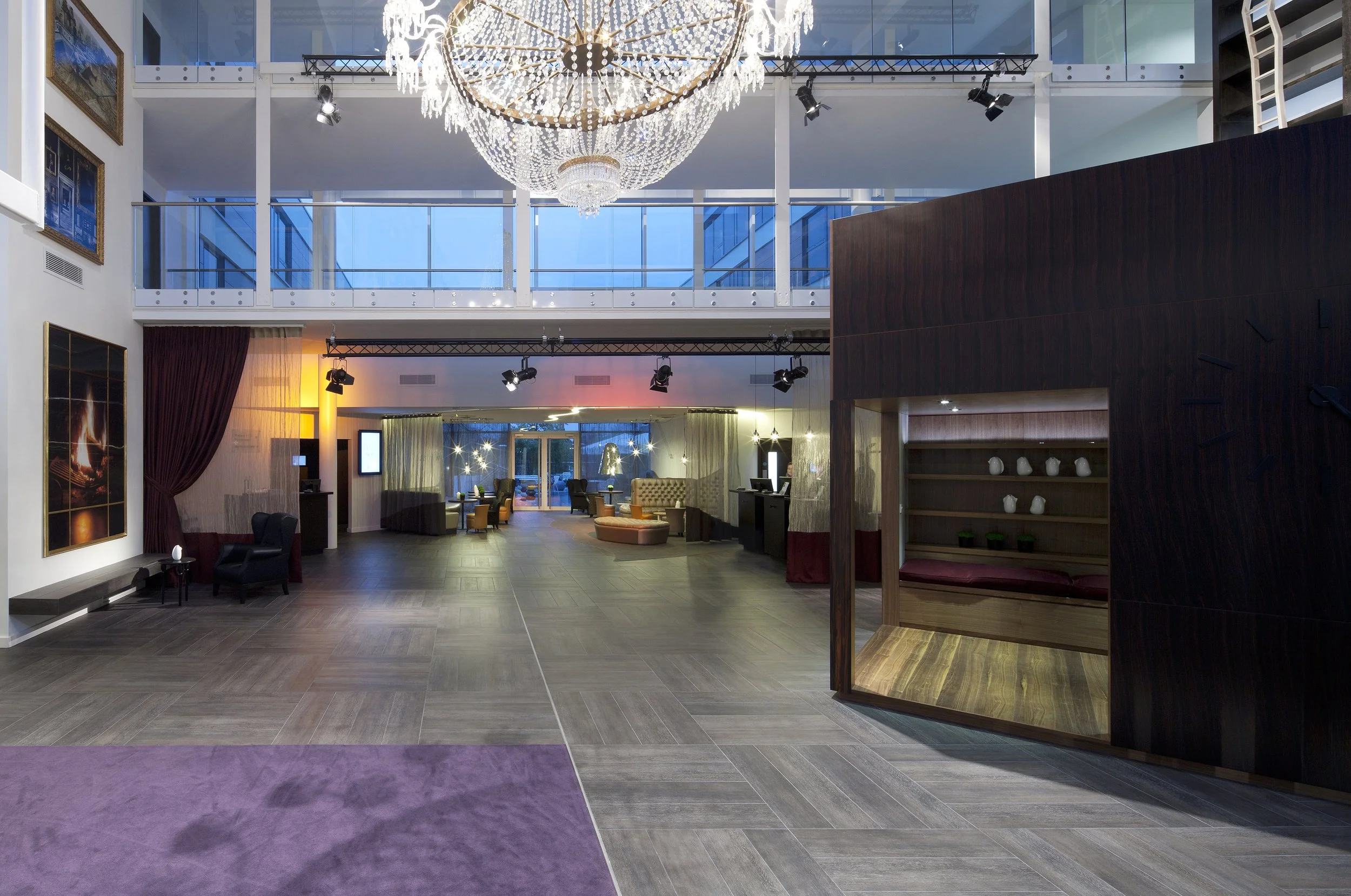 Interior or a large hotel lobby with a large crystal chandelier and other dramatic theatrical elements decorating the triple height volume.