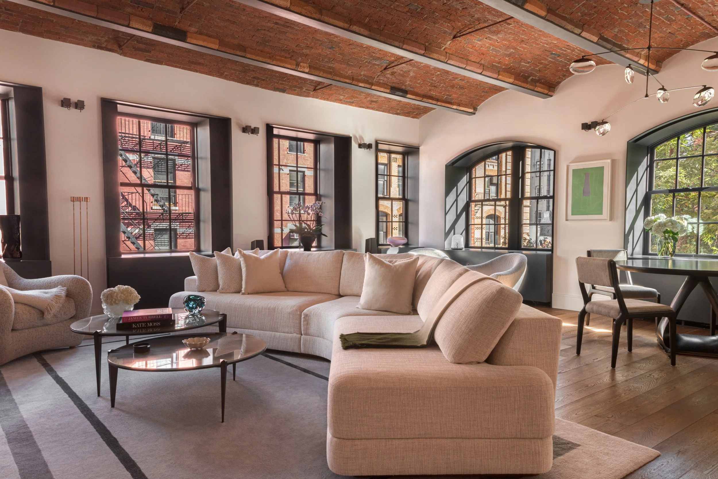 A wider interior view of the sitting areas and dining area of the apartment, with exposed brick ceiling vaults and many windows looking out over the NoHo new york city neighbourhood.