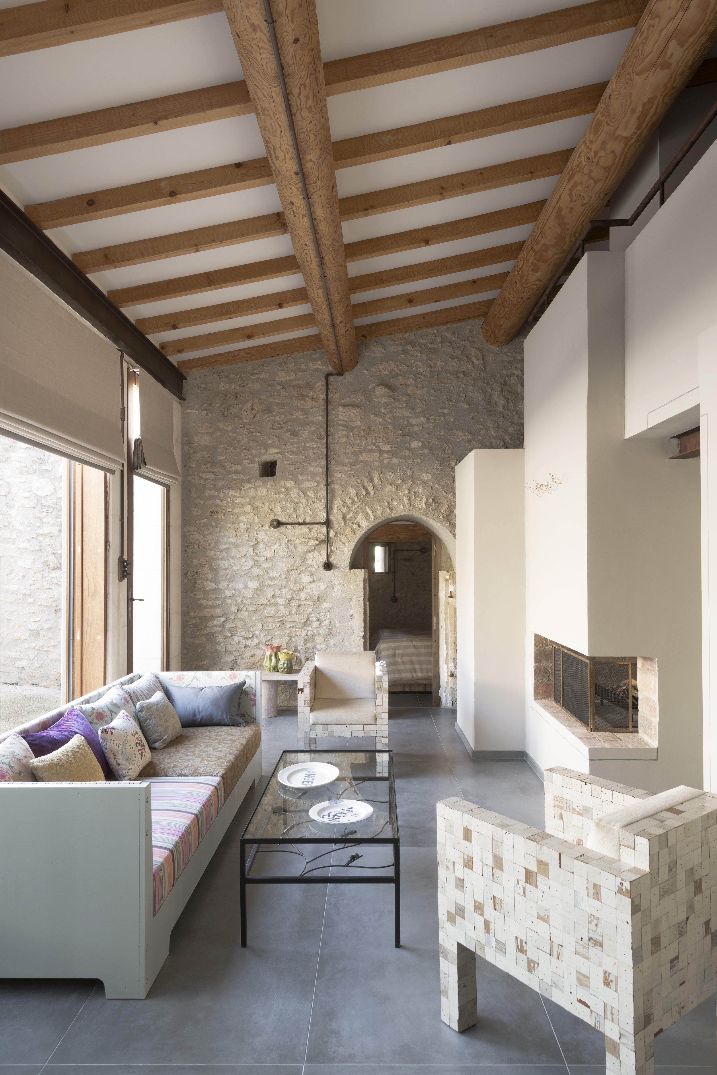 View of the living room with exposed stone wall at the far end, with an arched doorway lading to one of the ground floor bedrooms.