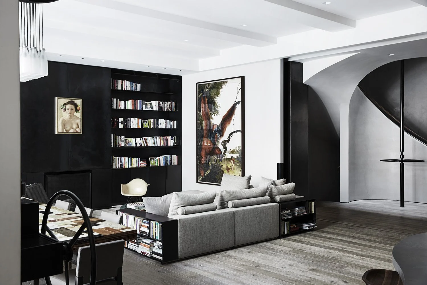 Interior image of a living room with patinated metal bookshelves and fireplace with a curving plaster staircase in the background.