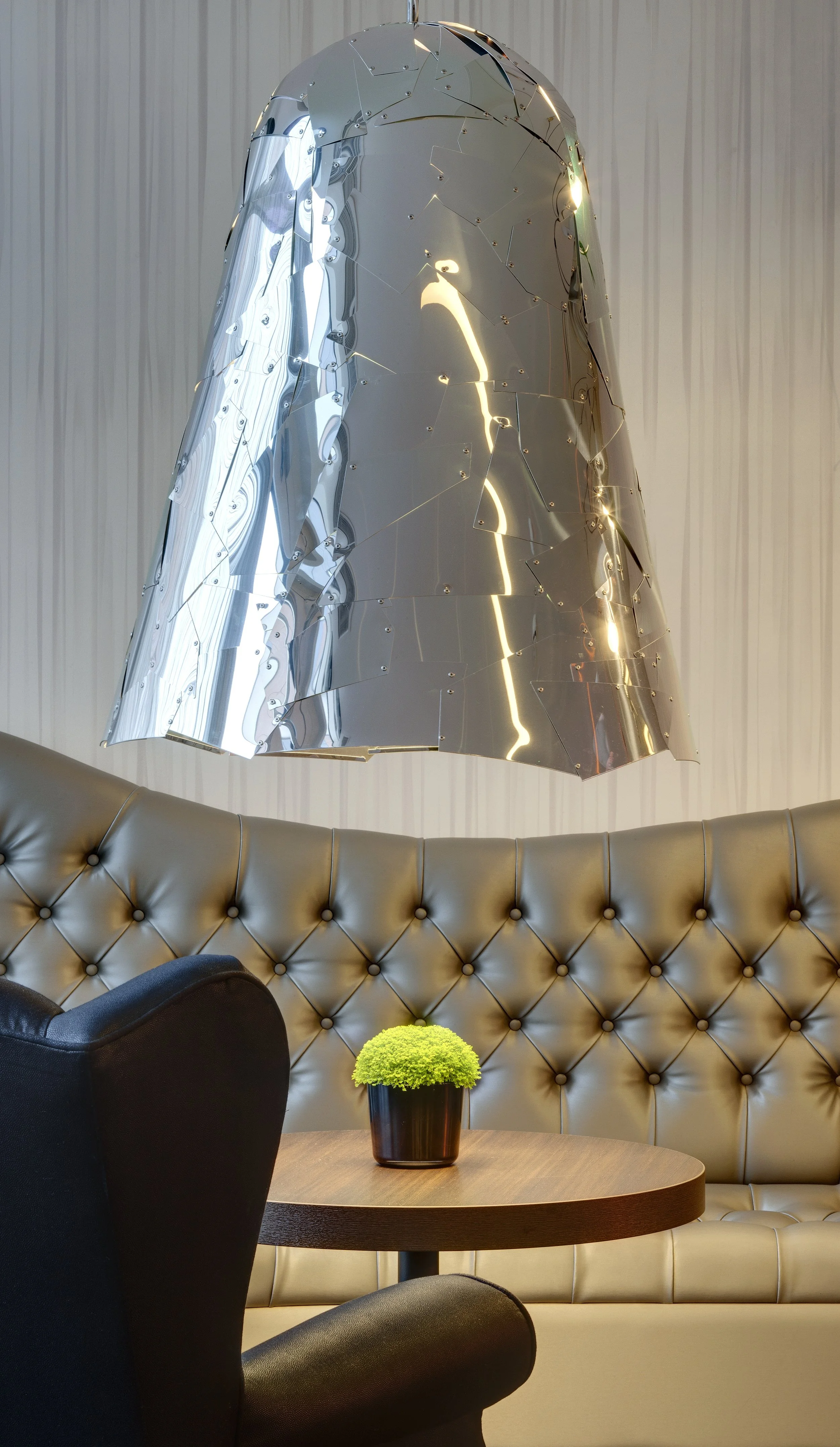 Detail interior photo of a buttoned banquette seating area with a patchwork polished steel oversized light fitting.