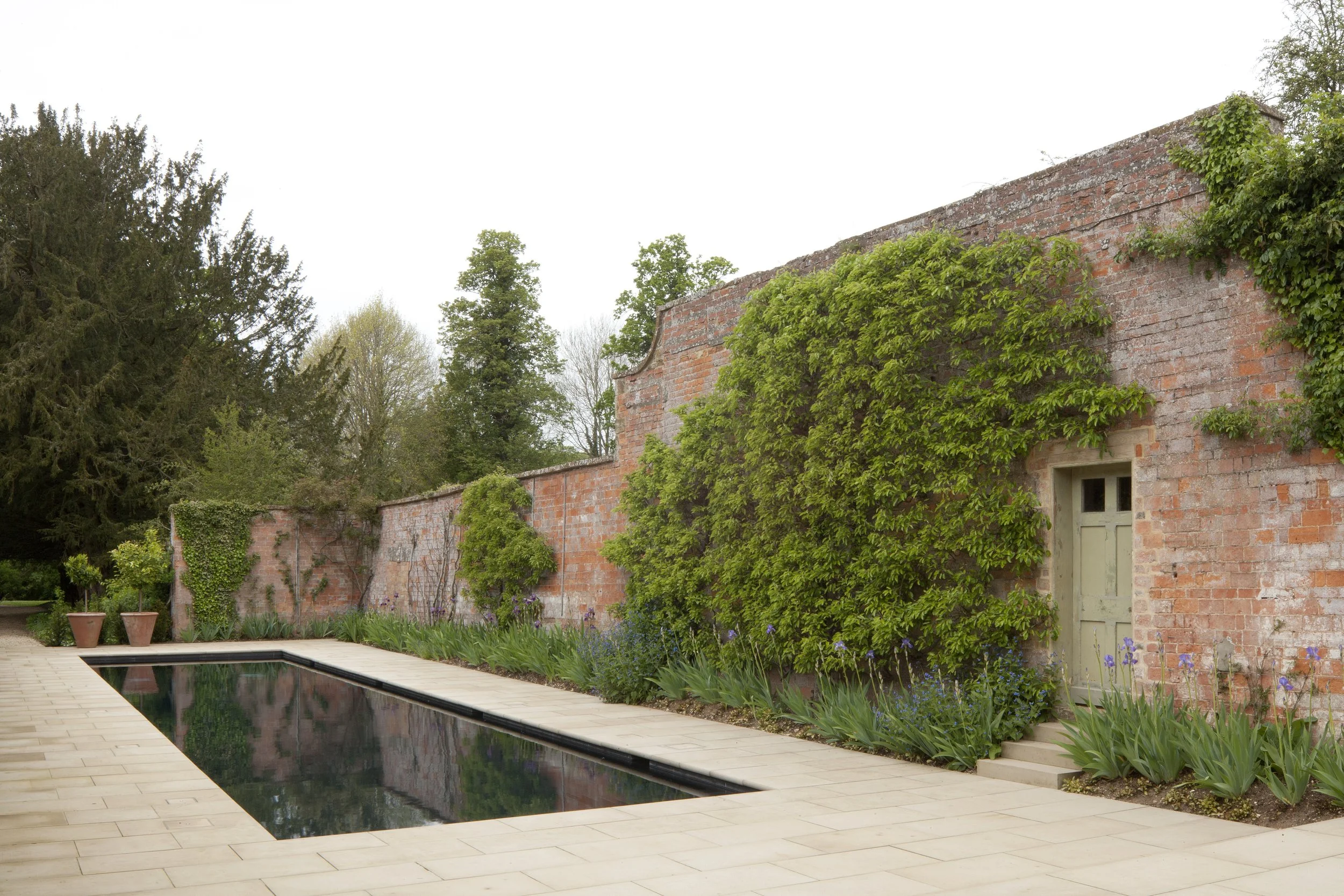 Image of a restored brick building turned pool house behind a dark pool with stone surround.