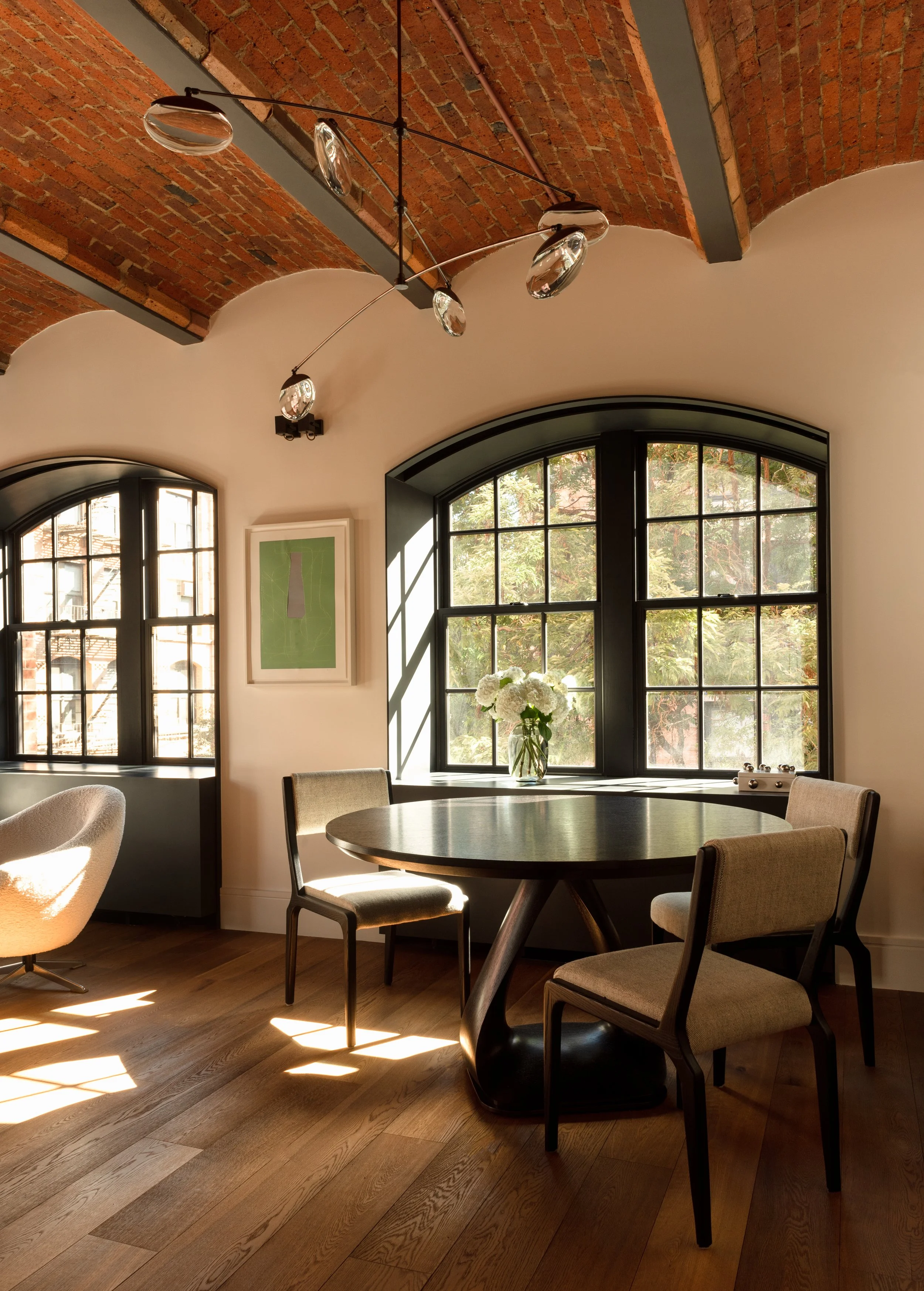 Interior photo of a stylish NoHo apartment with large arched windows looking out over a leafy New York City street.