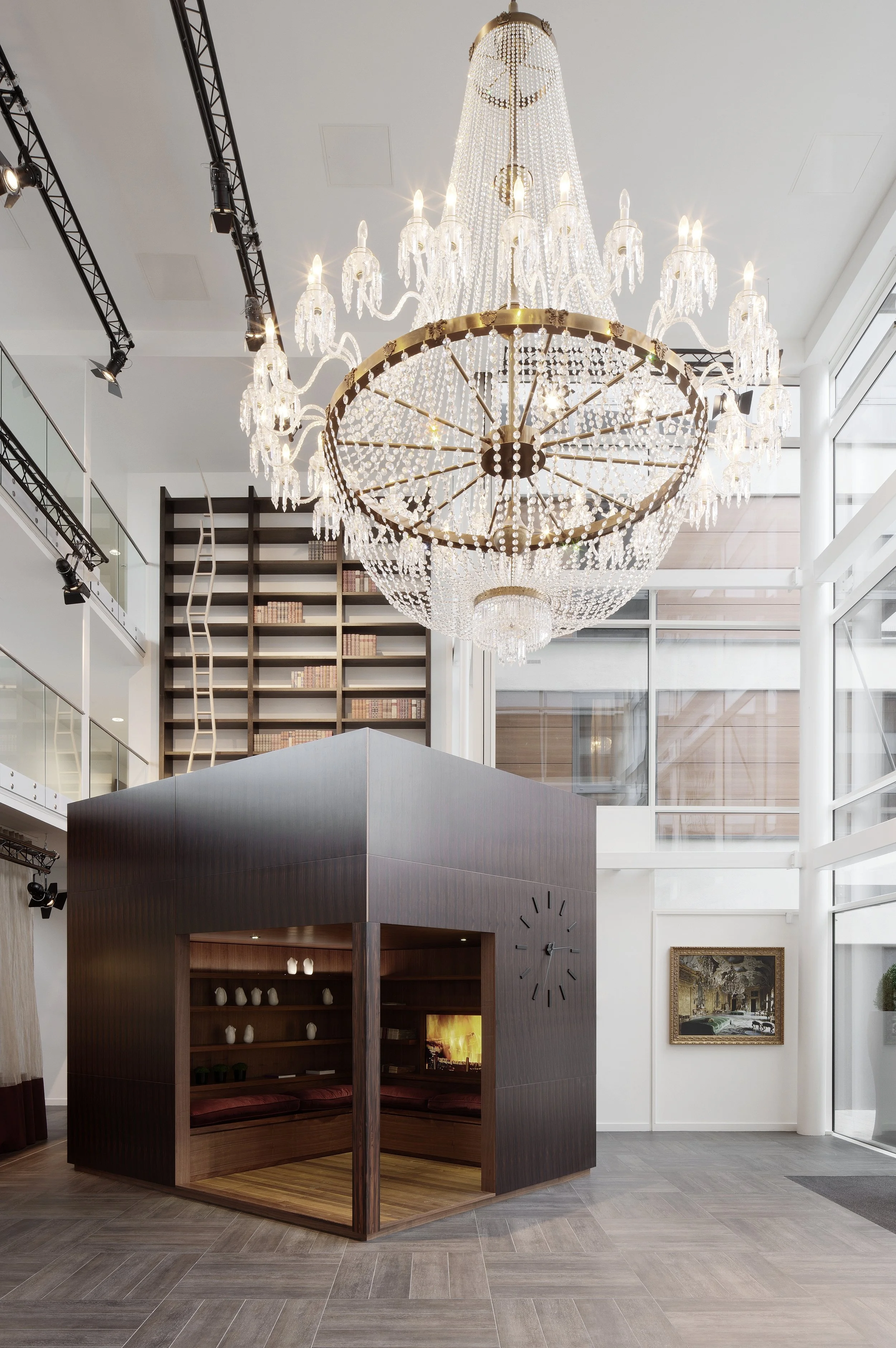 Interior view with the timber lobby cube with seating inside and a working station on top, accessible via stairs on the back.  Above is a massive crystal chandelier.