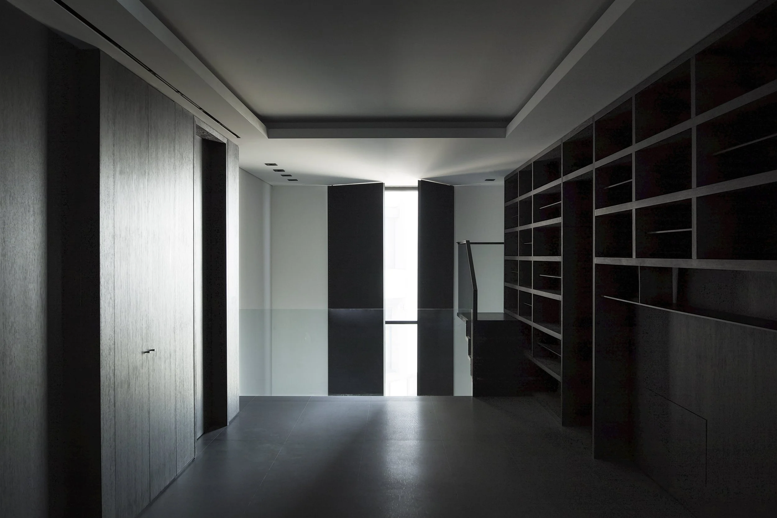 Interior image of a minimal space with dark wood bookshelves and monumental metal shutters.