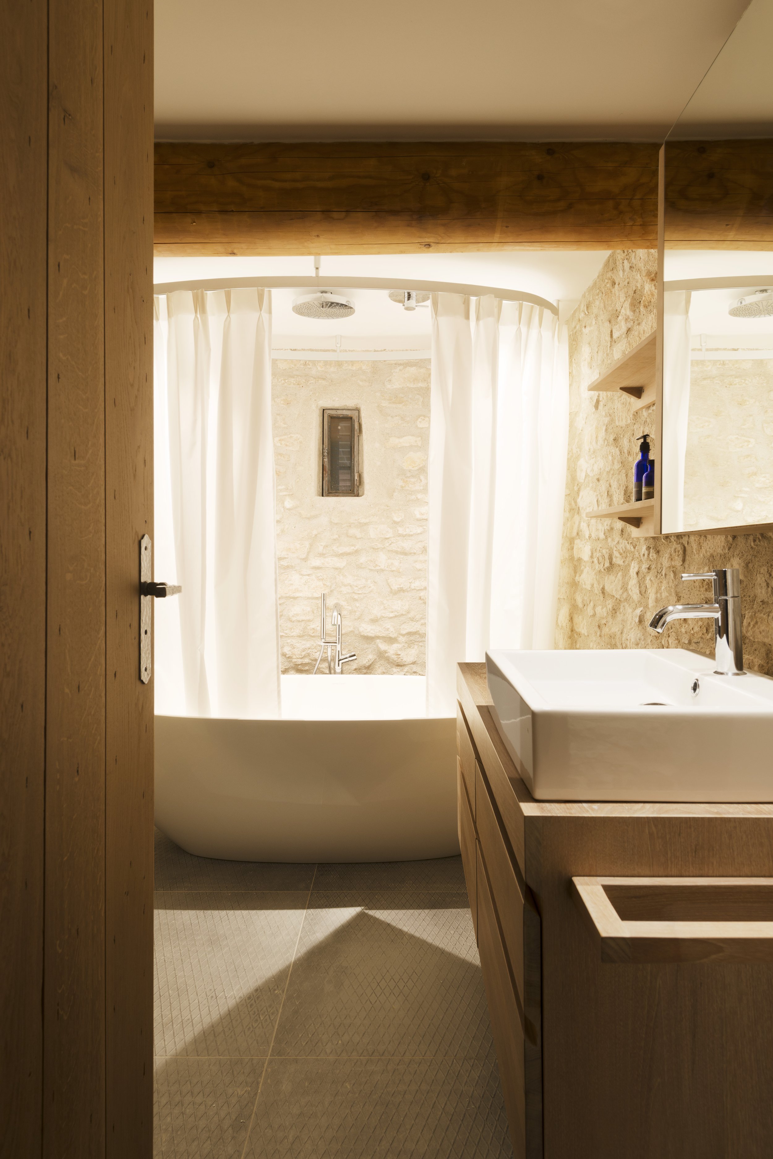 View of one of the bathrooms with a free-standing bath in front of one of the arrow-slit windows in the stone wall.