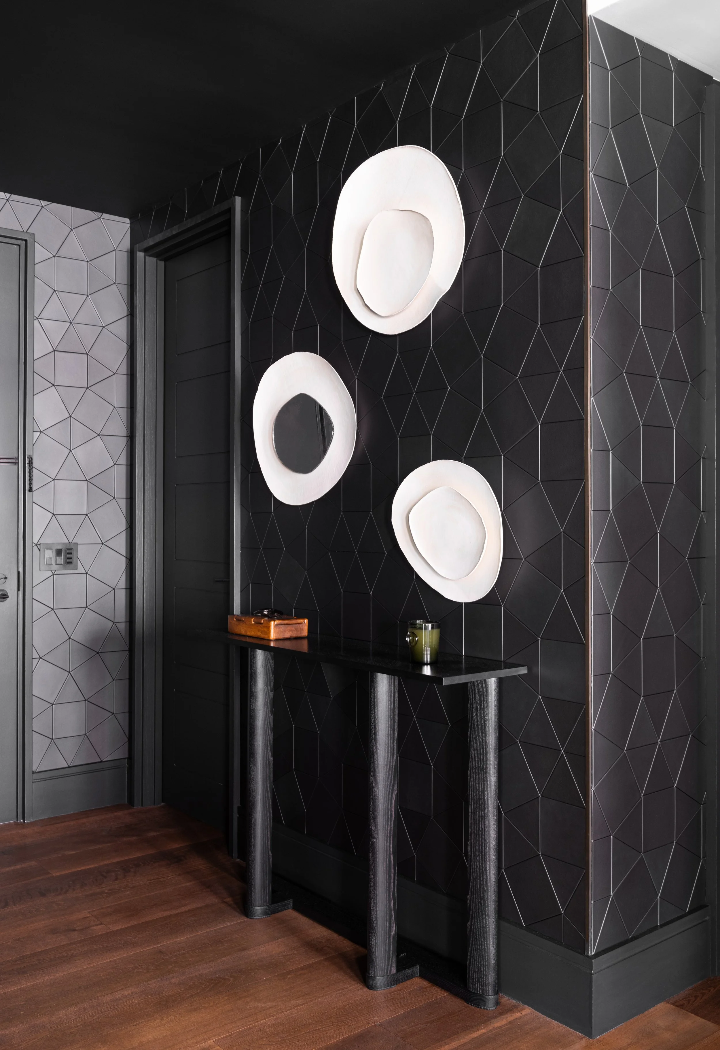 Interior photo of the dark-toned entry, with geometric, textured anthracite gray wallpaper, and a black stained wooden console table.