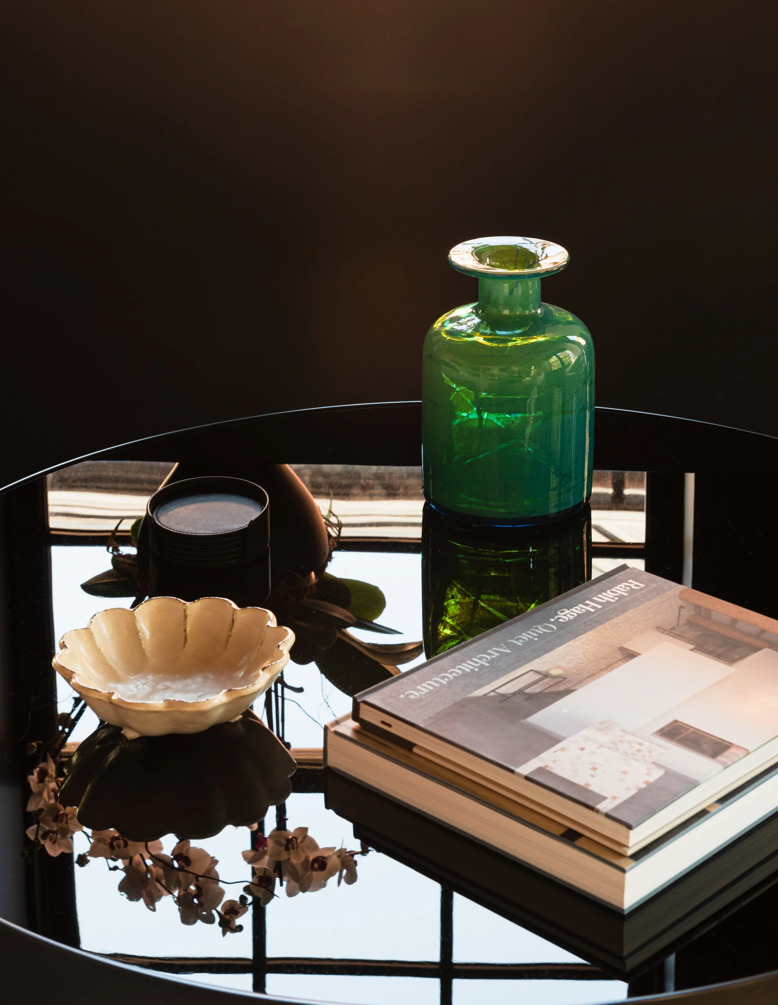 Detail interior photo of an occasional table showing a  collection of objects, books with the reflection of a window showing in the dark surface of the table.