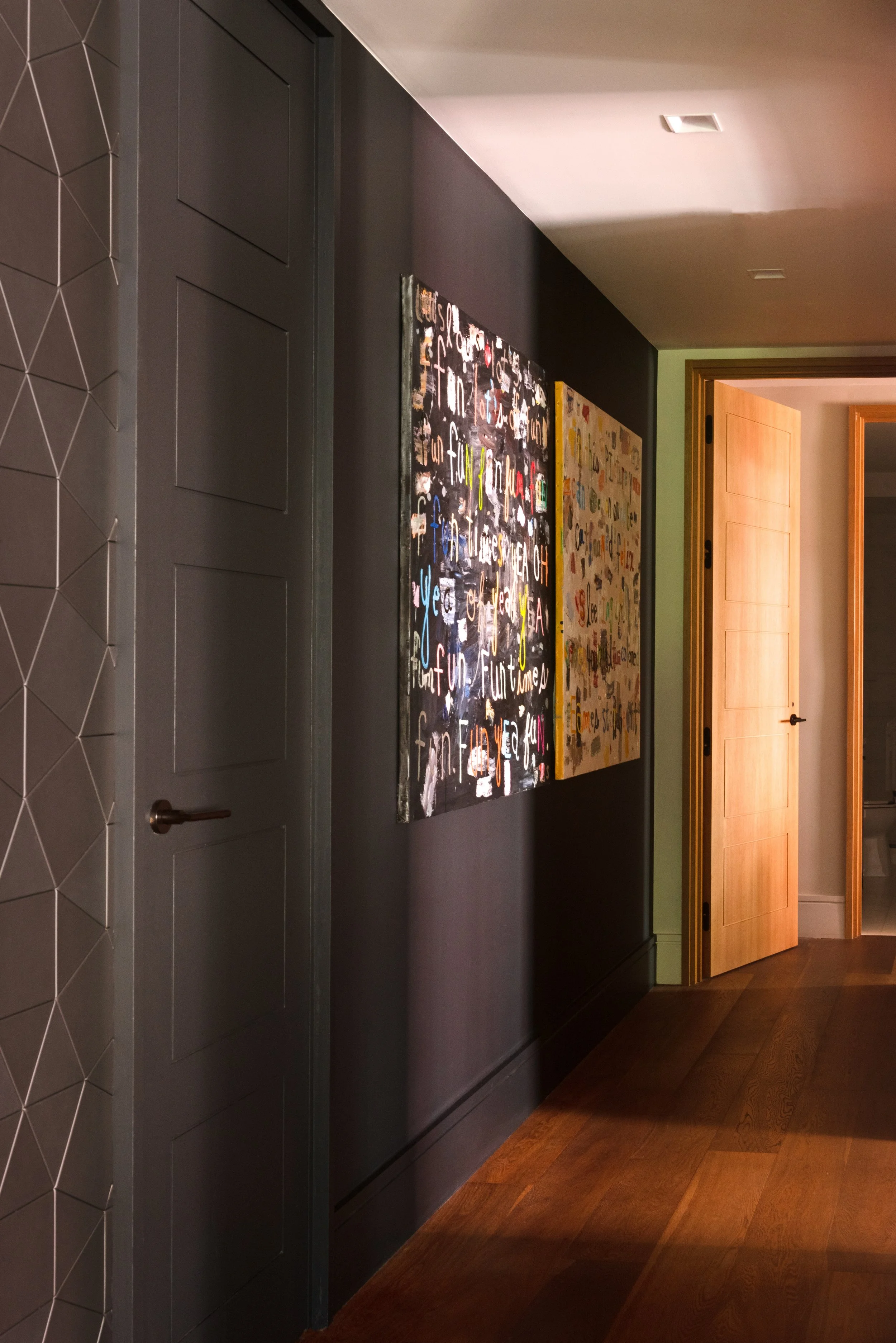 Interior photo of the hall leading to the bedrooms.  One wall is painted in the dark anthracite gray of the entry, with two text-based paintings by Susan Shup.