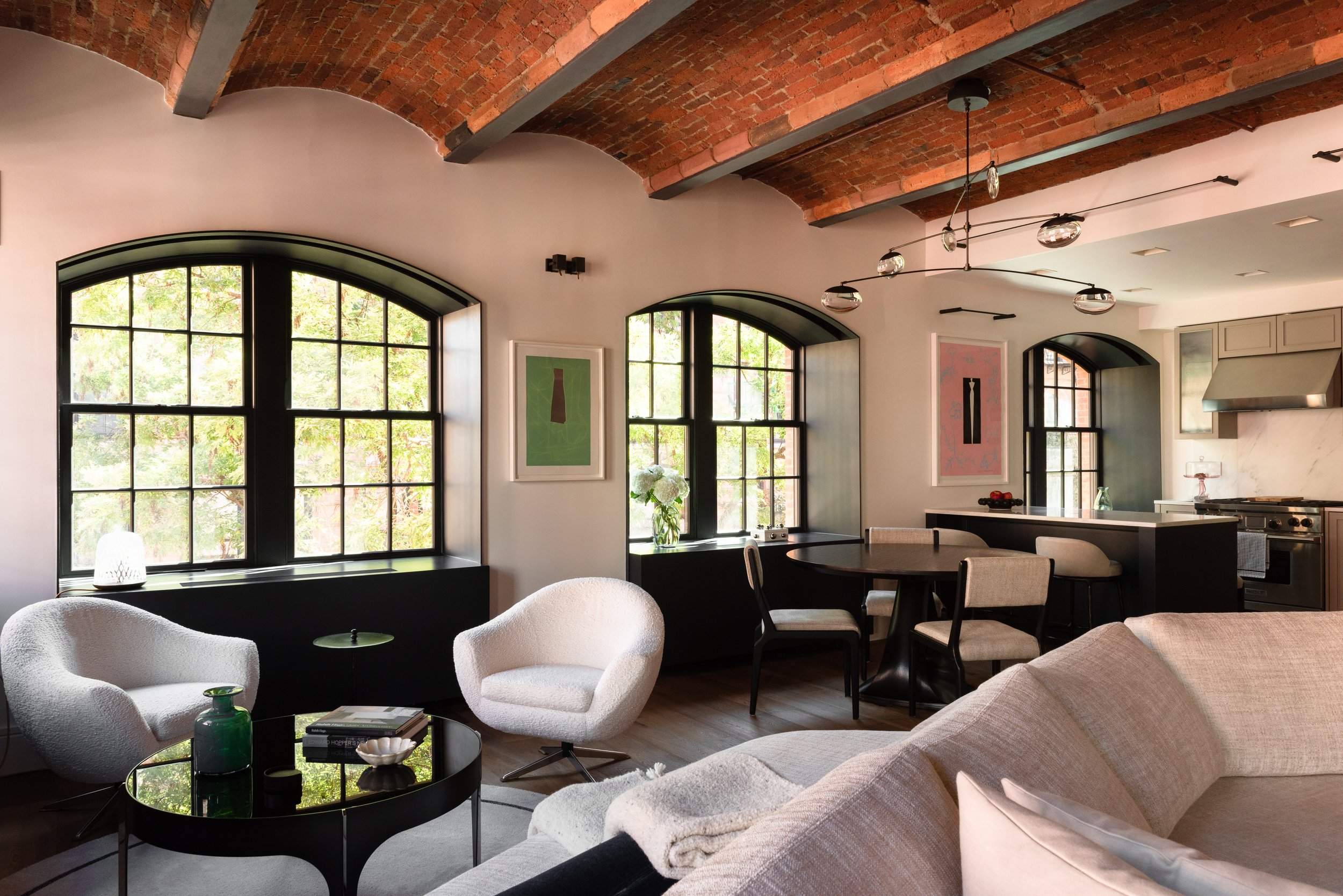 Wide interior photo of the relaxed sitting area in front of the large arched windows, beneath the exposed brick ceiling vaults. To the right is the dining area and kitchen.