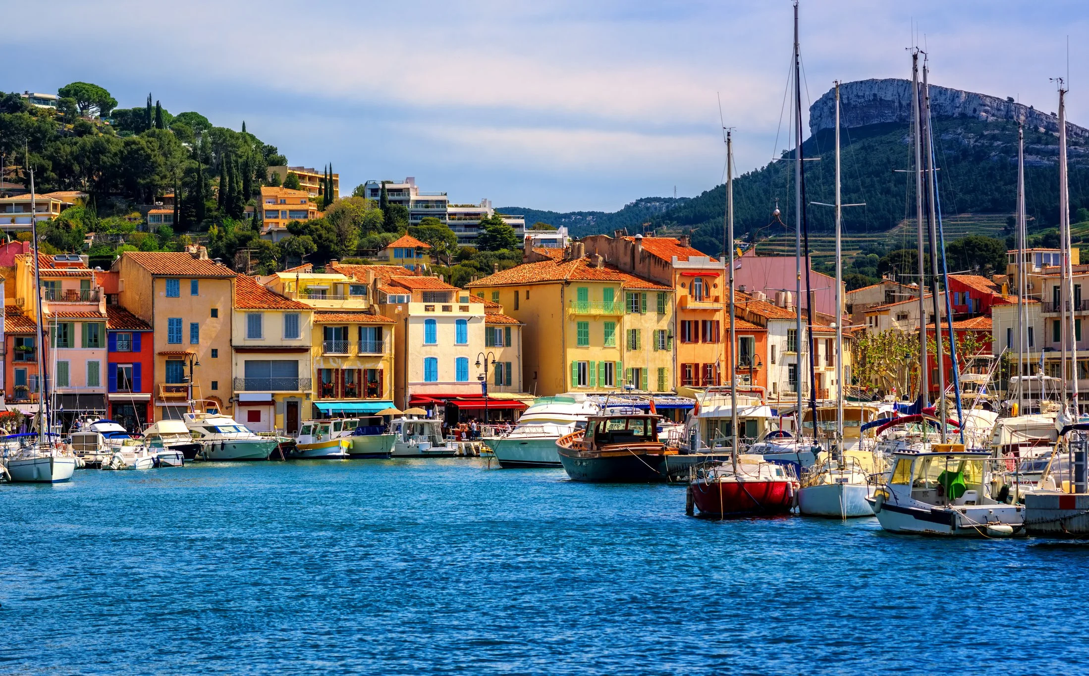 Colorful buildings along a marina with boats docked at the waterfront, with hills and a mountain in the background.