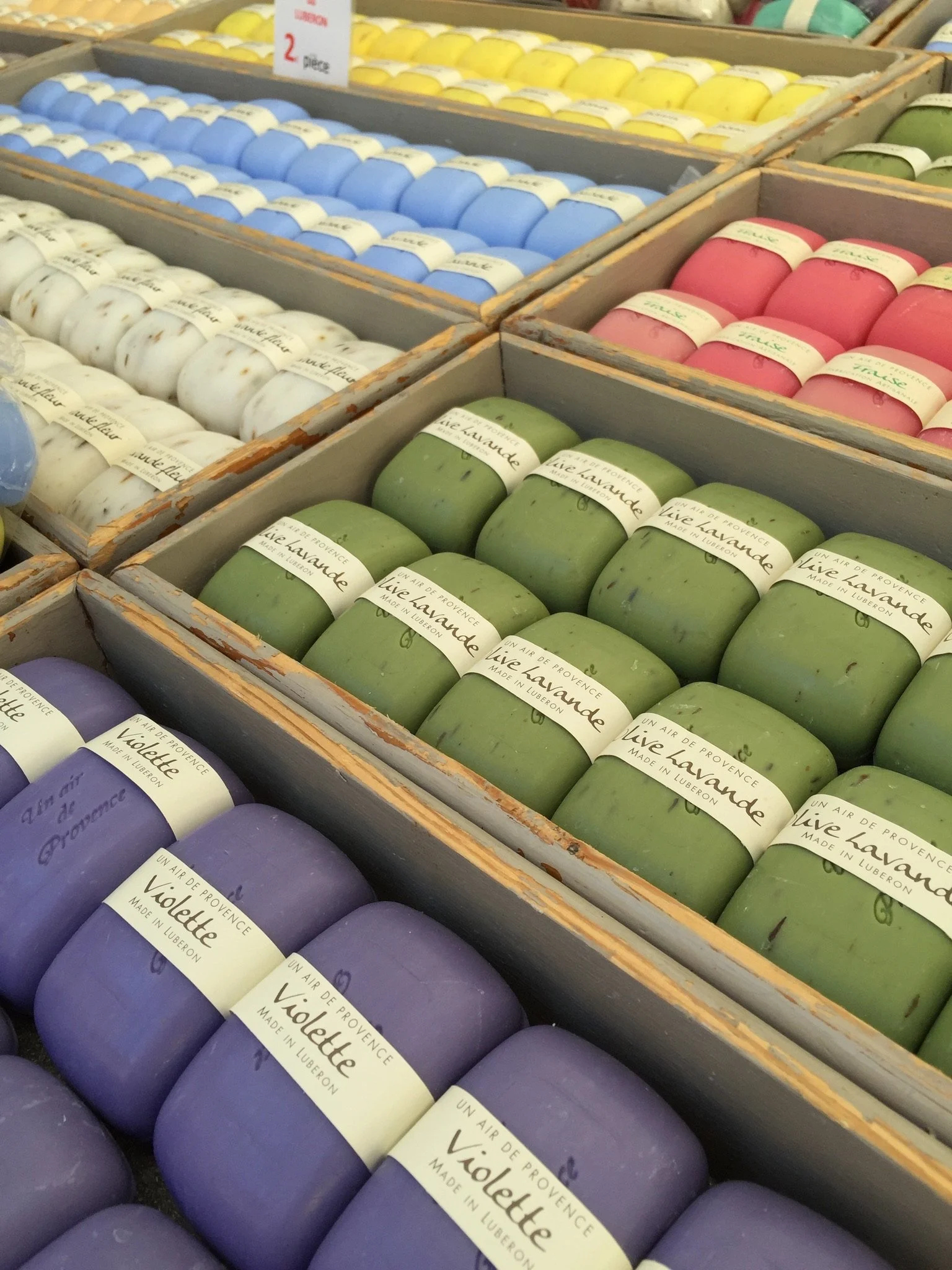 Colorful candles with labels that say 'Violette' and 'Live Lavande,' arranged in wooden boxes at a store.