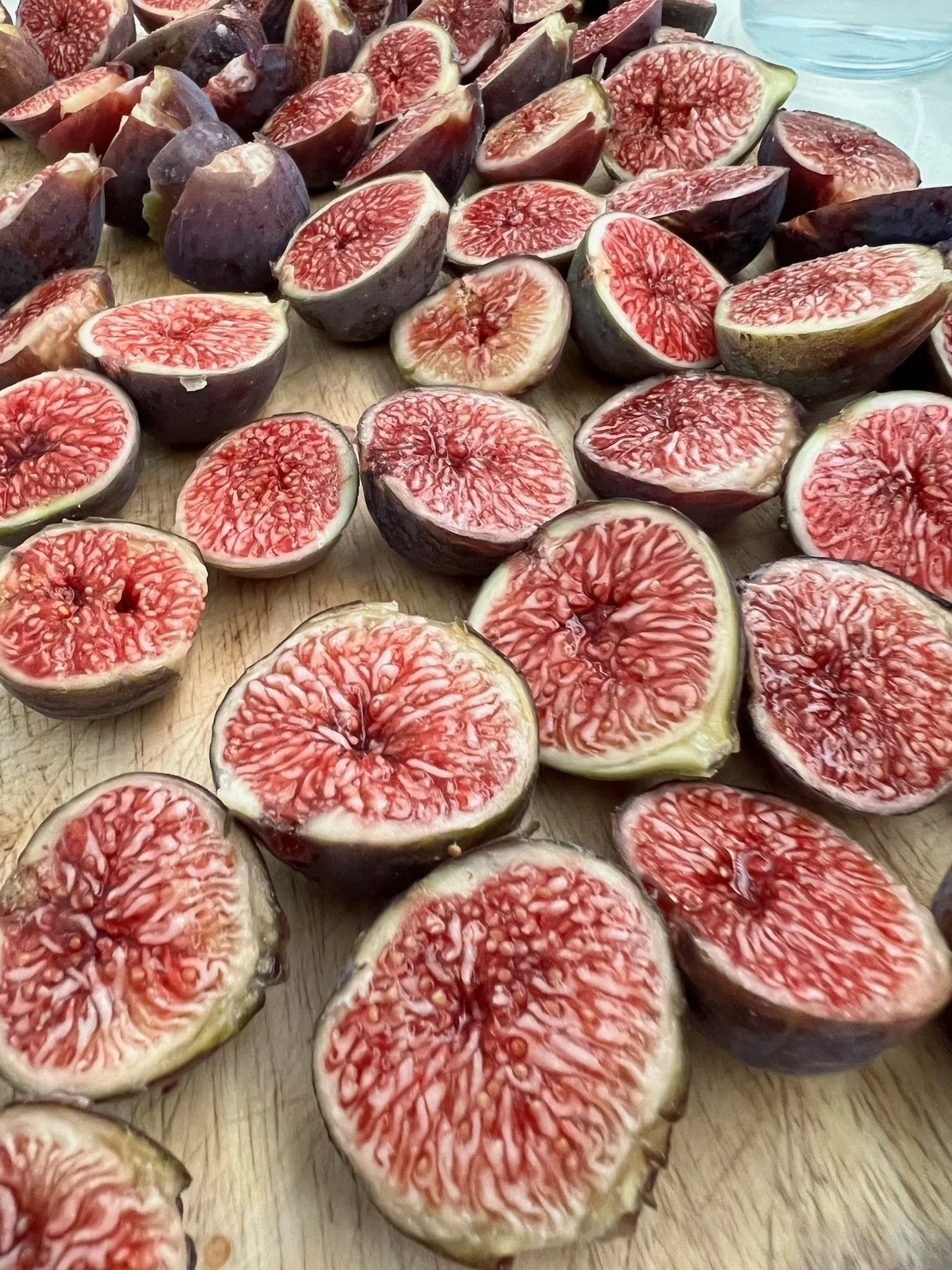 Several halved ripe figs with red flesh and purple skin on a wooden surface.