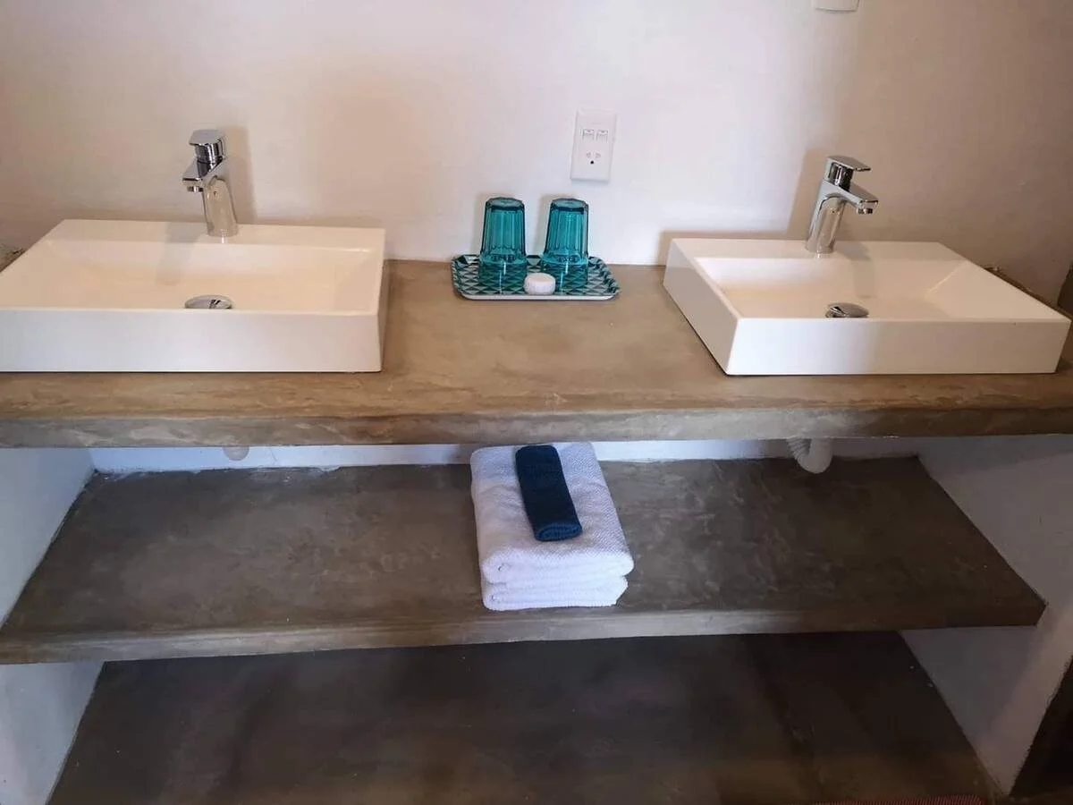 Double bathroom vanity with two rectangular white sinks, two faucets, a tray with two glasses, and towels underneath.
