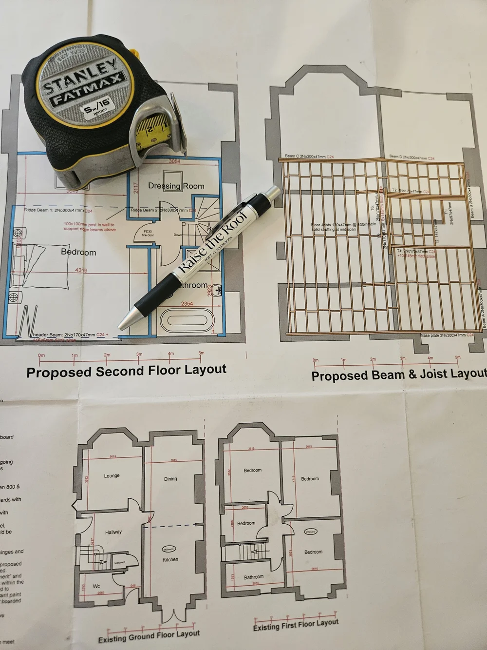 Architectural plans of a house's second floor and beam layout, with a measuring tape and marker on top.