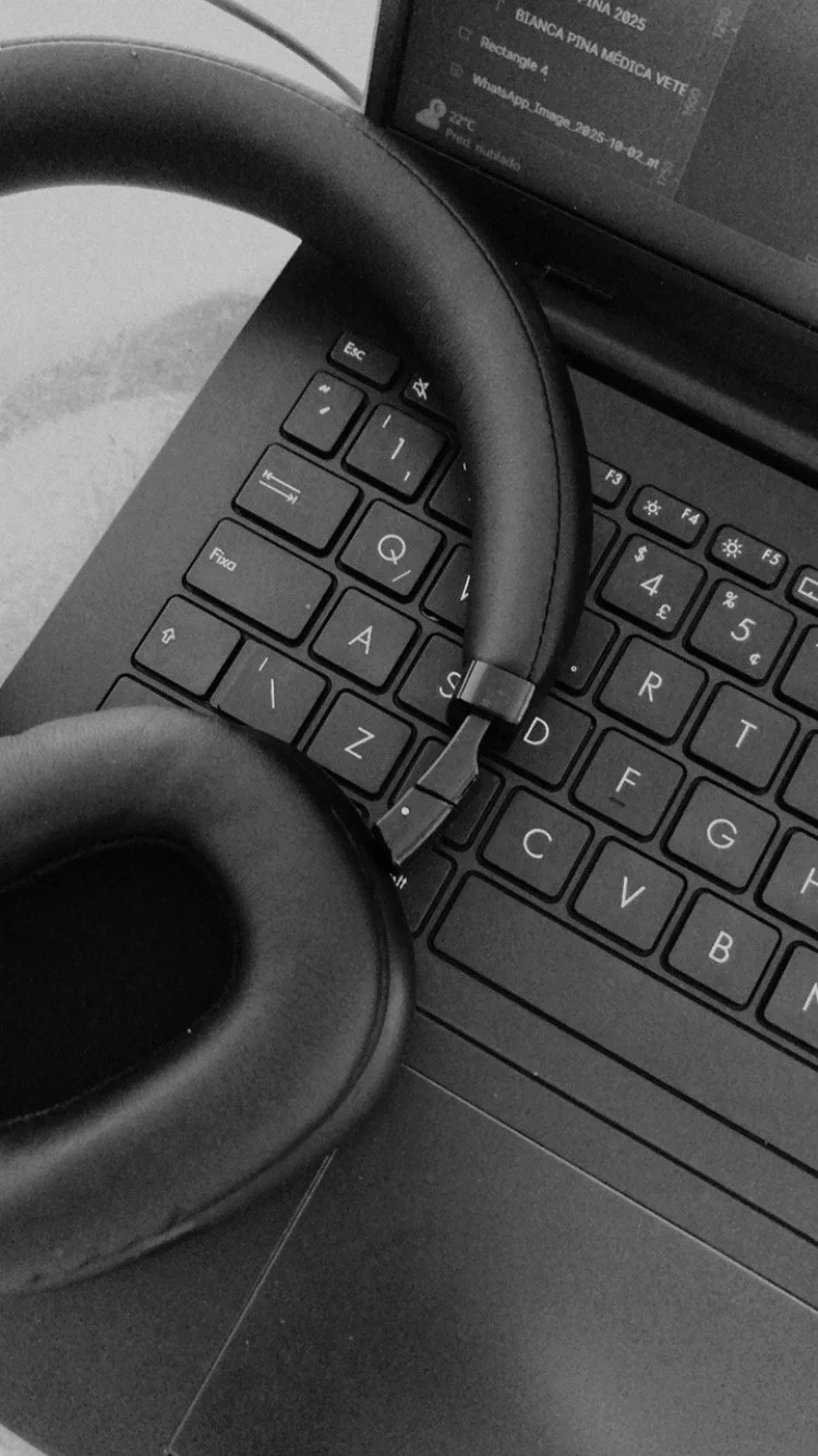 A black and white photograph of a laptop keyboard with a pair of headphones resting on it. The laptop screen is partially visible, showing some text and icons.