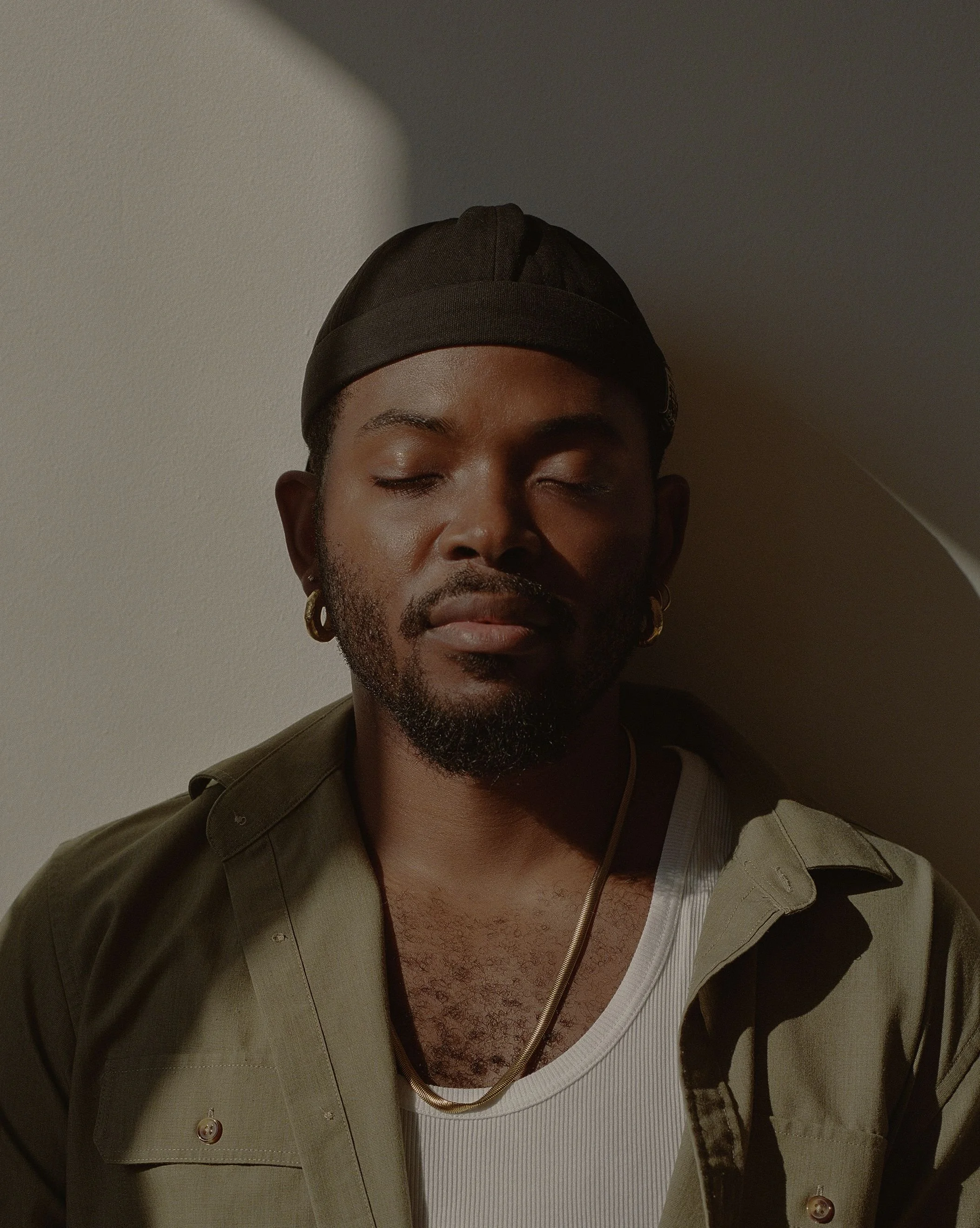 Keanu Jackson LCSW sits before the camera in a durag and an olive green button-up shirt and gold hoop earrings. He is closing his eyes and his face is in a peaceful expression.