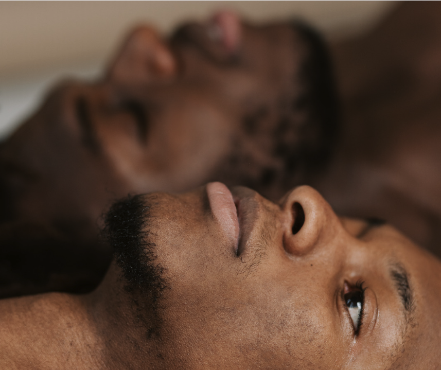 Two Black men lie on the ground next to one another facing opposite directions