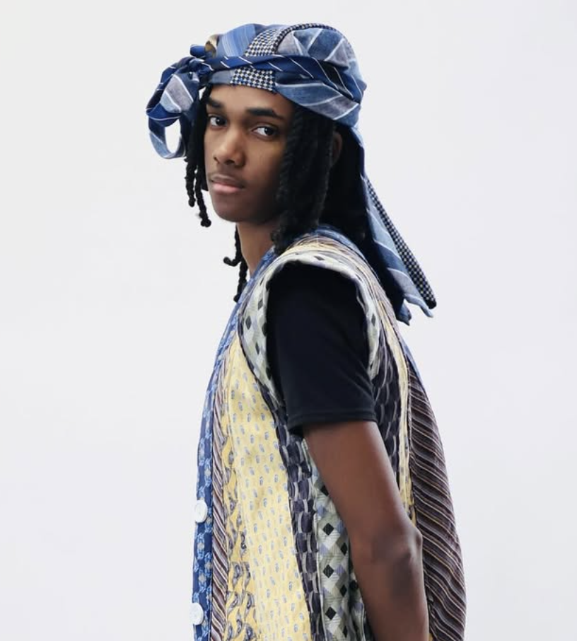 Young man wearing a blue patterned headscarf and colorful patchwork vest over a black shirt