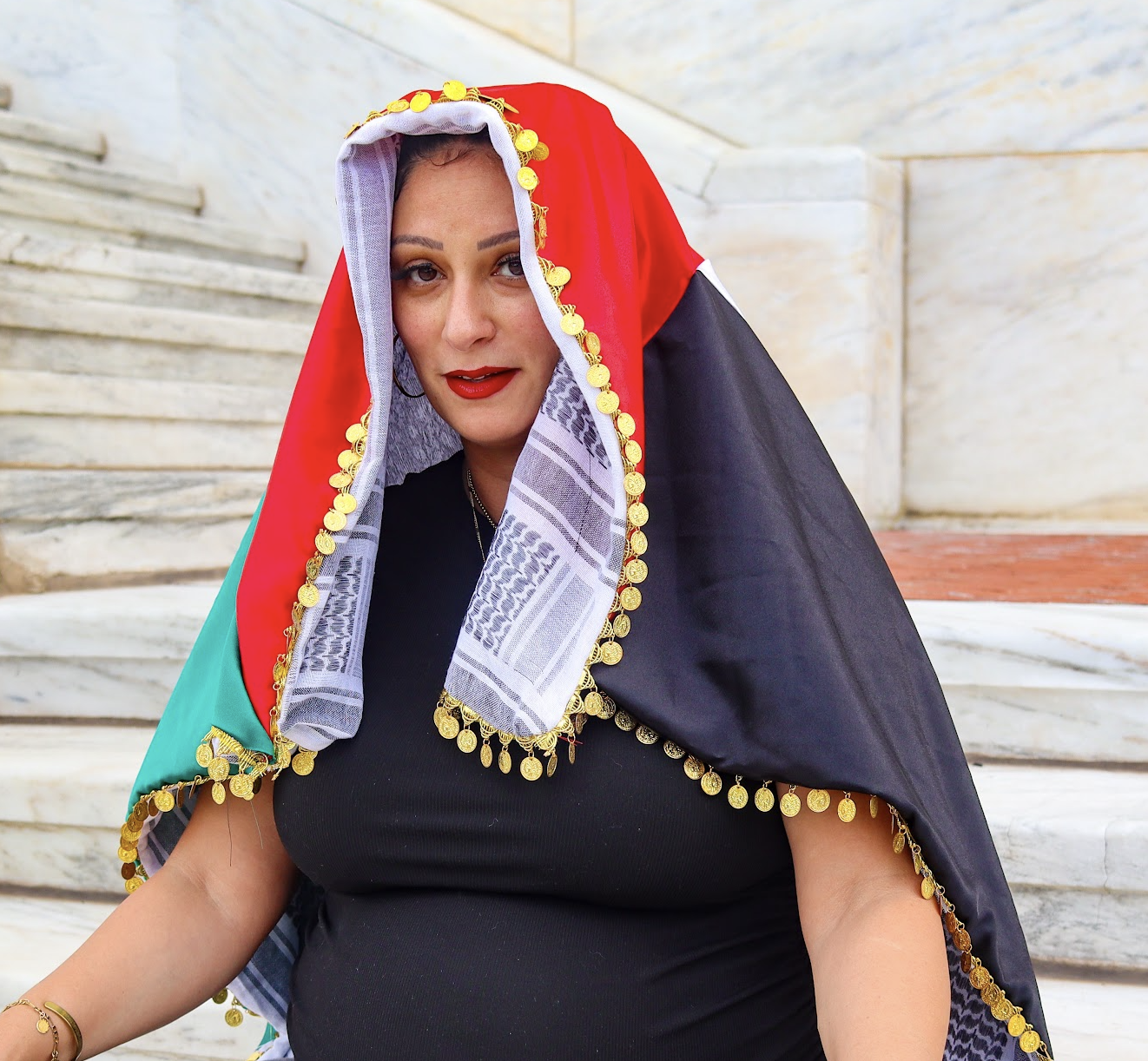 Woman wearing a traditional black, red, and teal coin-trimmed headscarf on marble steps