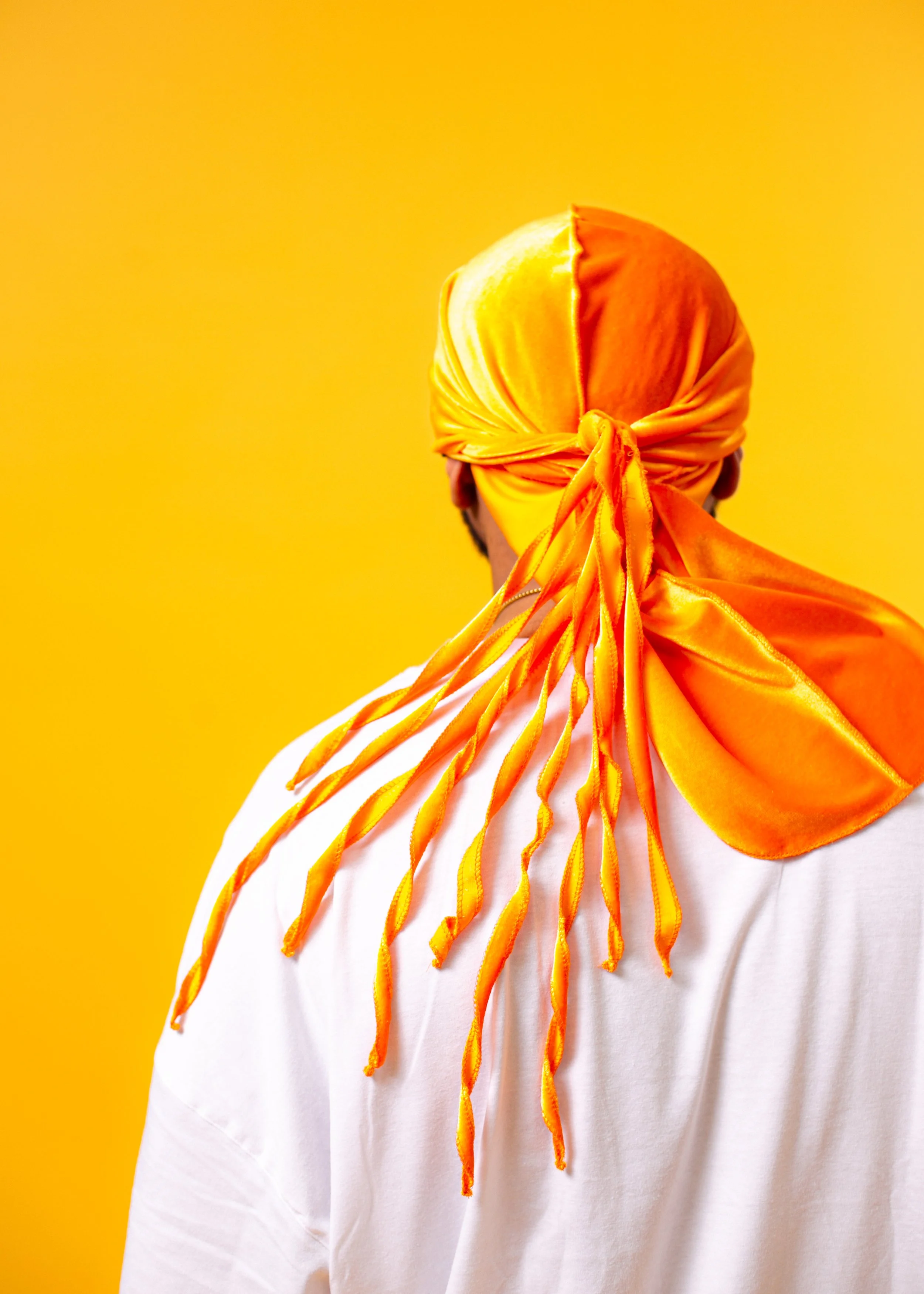 Person in a white shirt with an orange blindfold and tied fabric against a yellow background