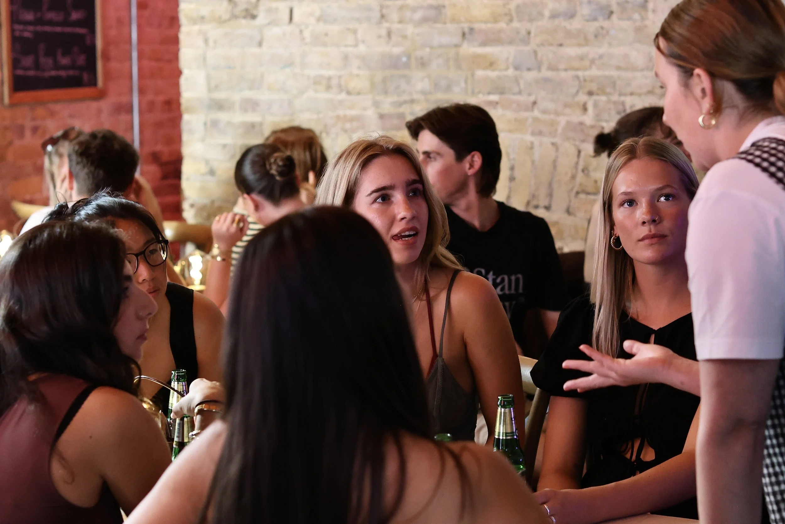 Group of young women sitting at a table in Khao Bird having a conversation, with a team member standing and talking to them.