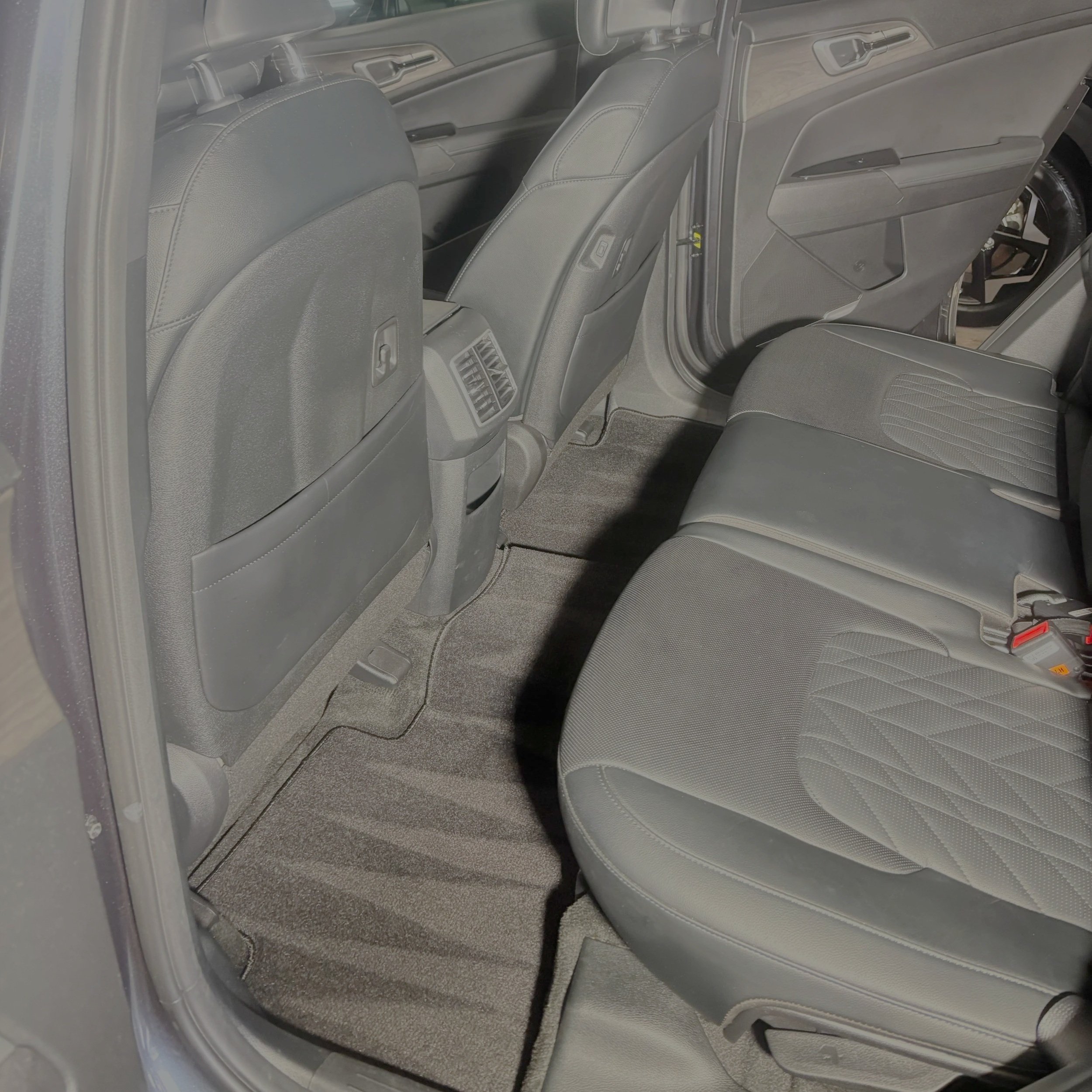 The image shows the interior of a vehicle, focusing on the back seat area with gray fabric seats and the back of the front seats, as well as the floor mat.