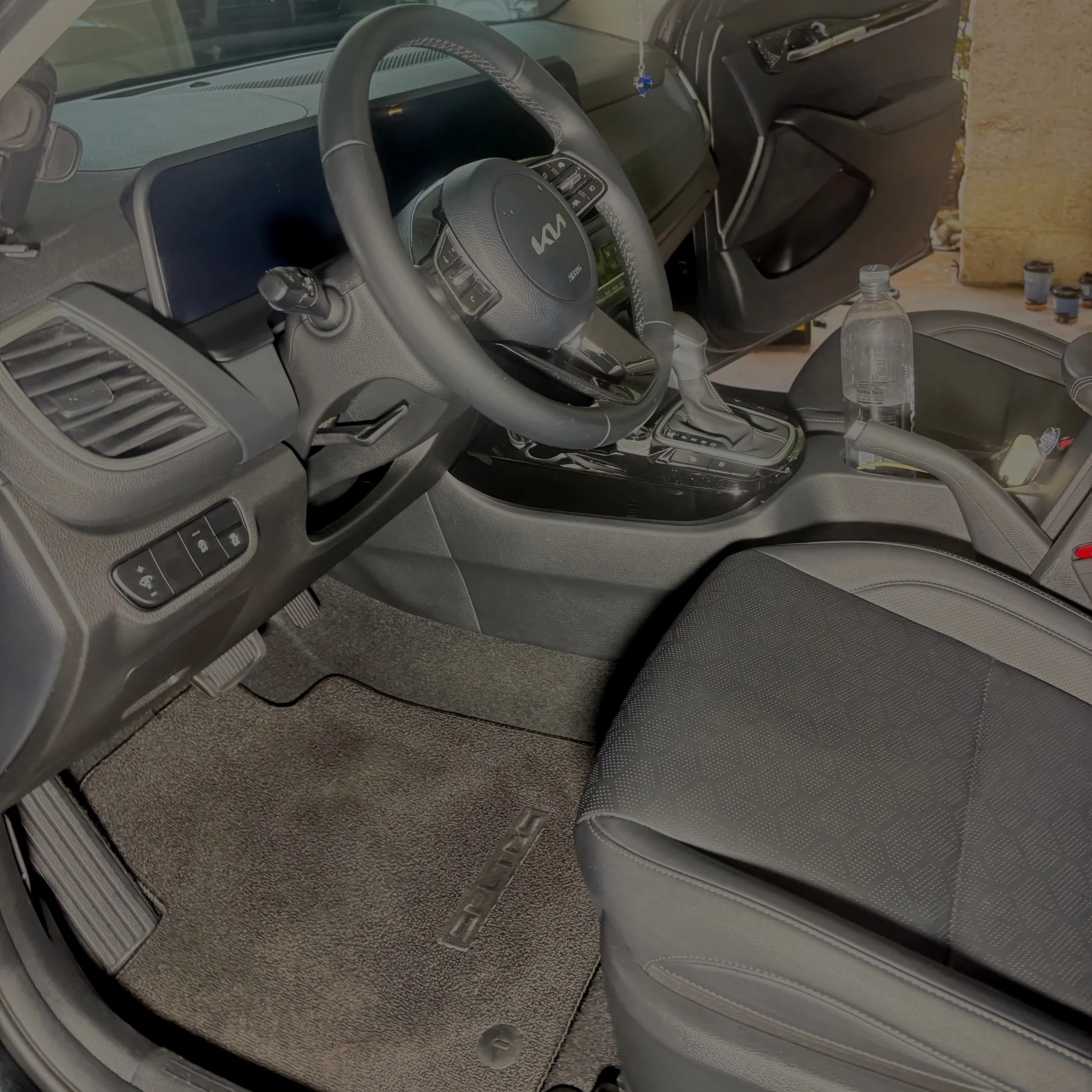 The interior of a car, showing the steering wheel, dashboard, gear shift, and driver's seat with a water bottle placed on the center console.