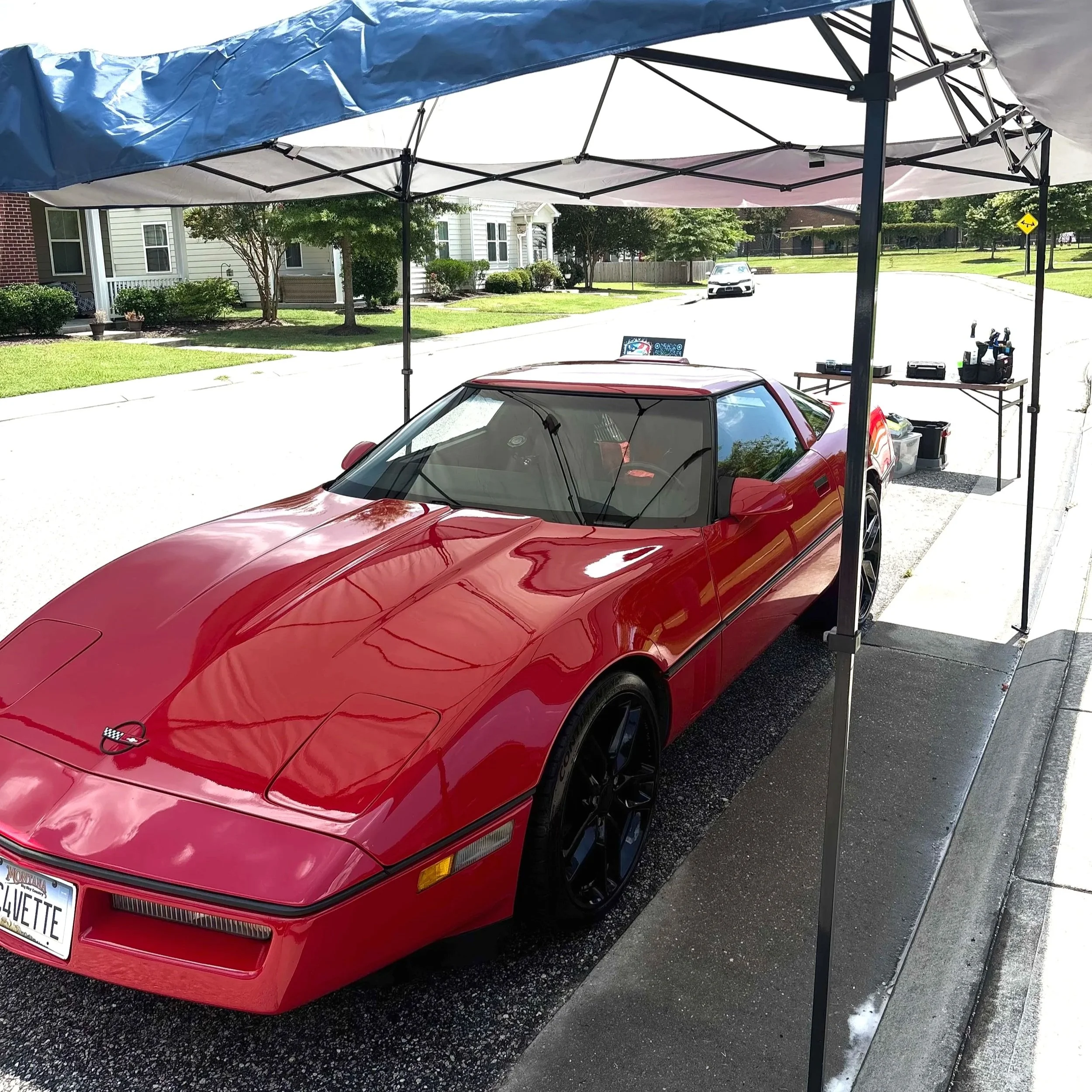 Red Chevrolet Corvette parked under a canopy with a work table and tools nearby.