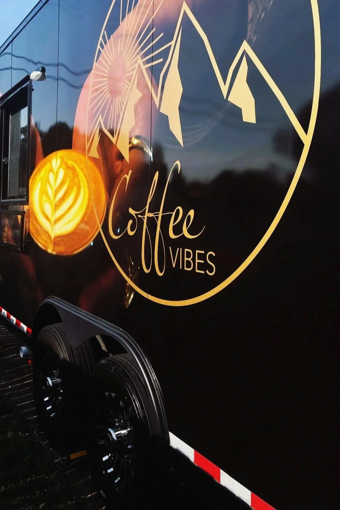 Black food truck with yellow and orange designs, a logo with mountains and sun rays, and the text 'Coffee Vibes'