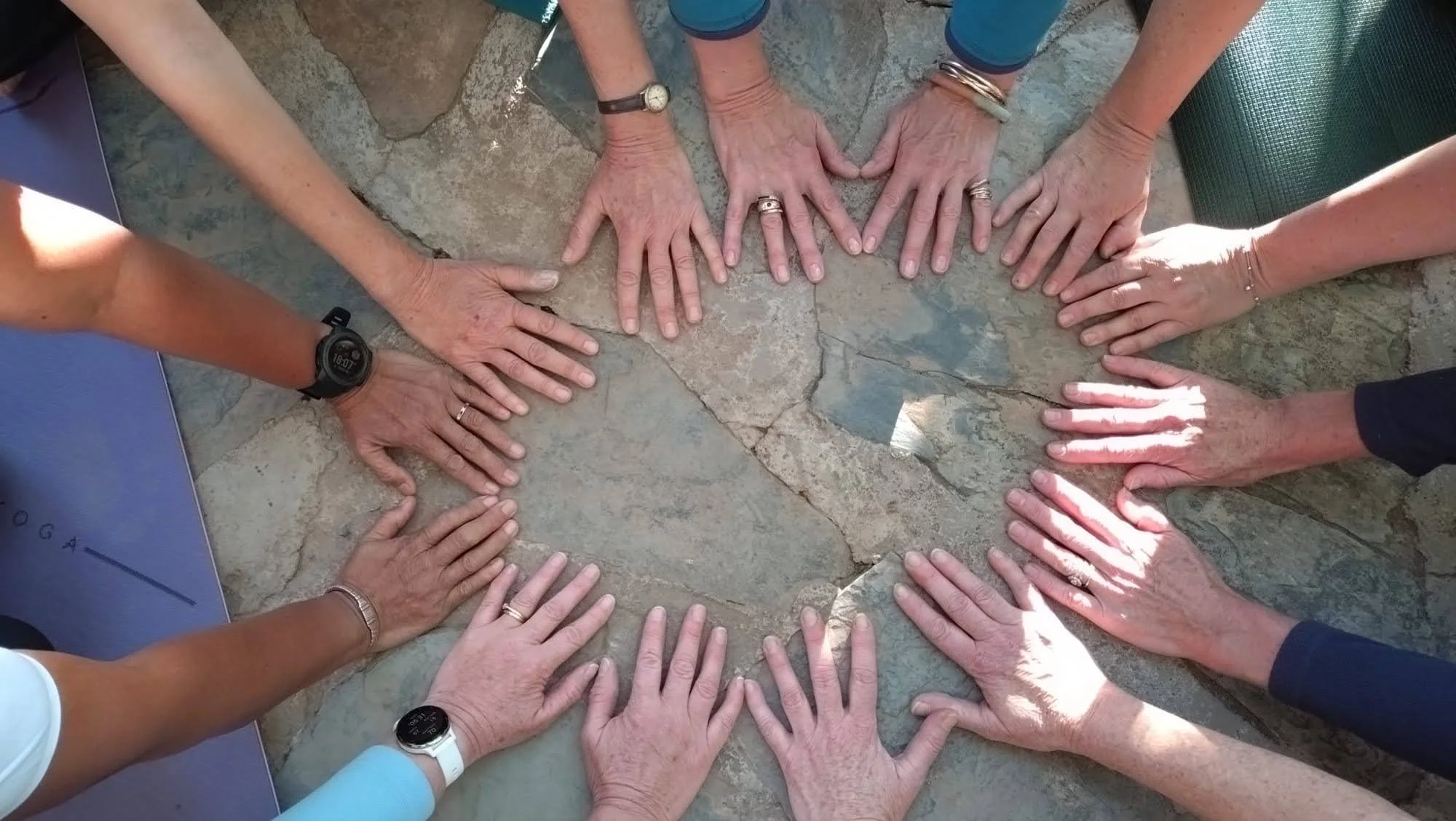 Multiple people with various skin tones have their hands placed together on a stone surface, forming a heart shape.