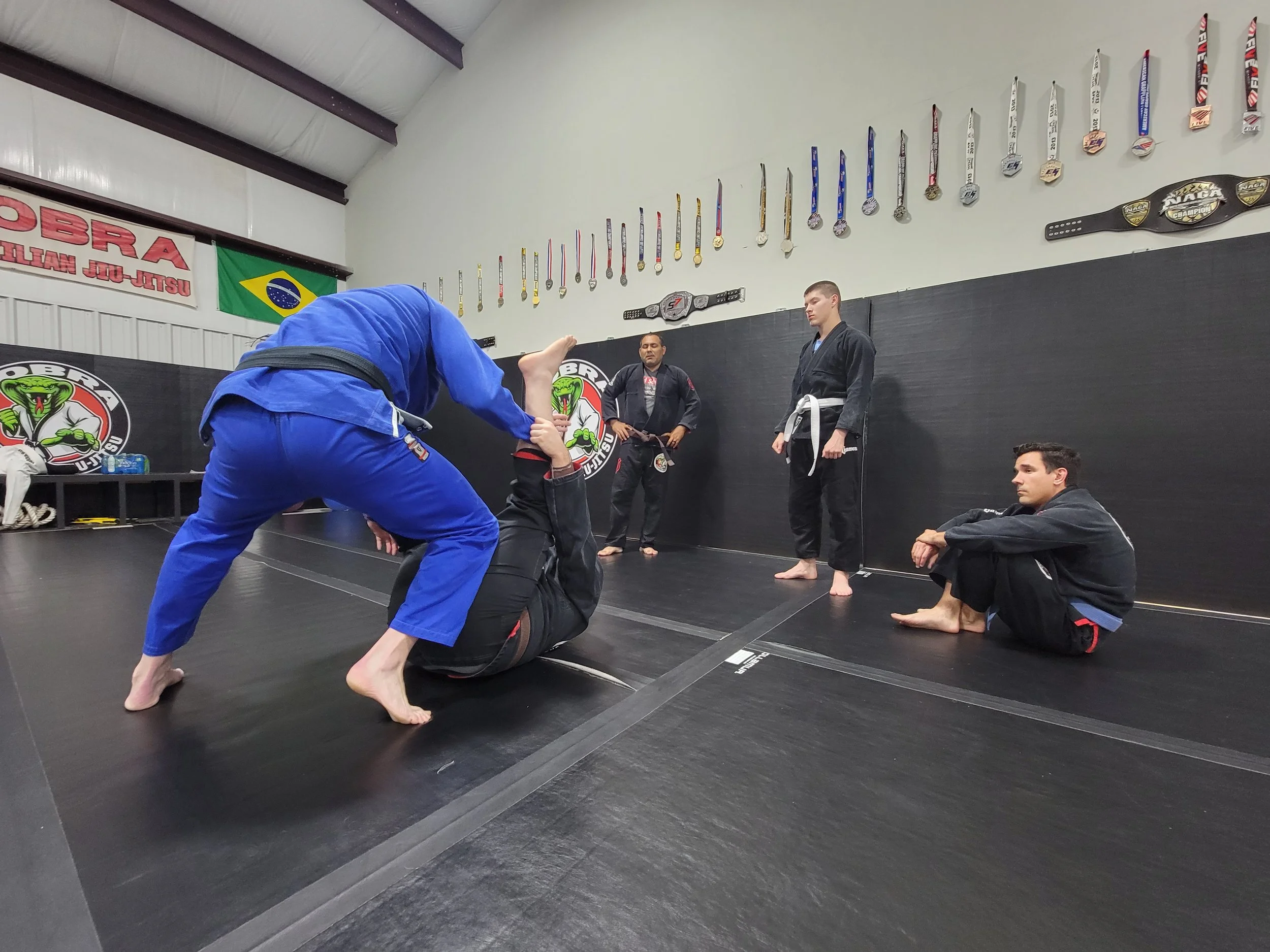 A student in a blue gi passing guard during an adult class at Cobra BJJ Mansfield