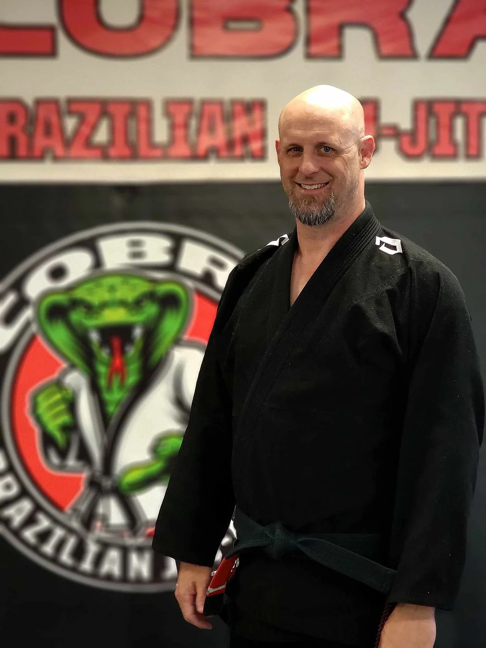 Chris Scott, second degree black belt, standing in front of the Cobra BJJ wall logo
