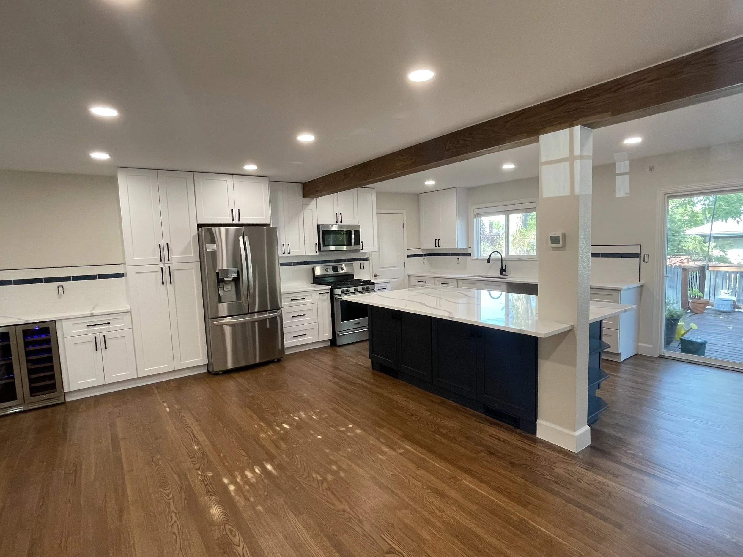 Modern kitchen with white cabinets, stainless steel appliances, a black island with white marble countertop, hardwood floors, and a sliding glass door leading to an outdoor deck.