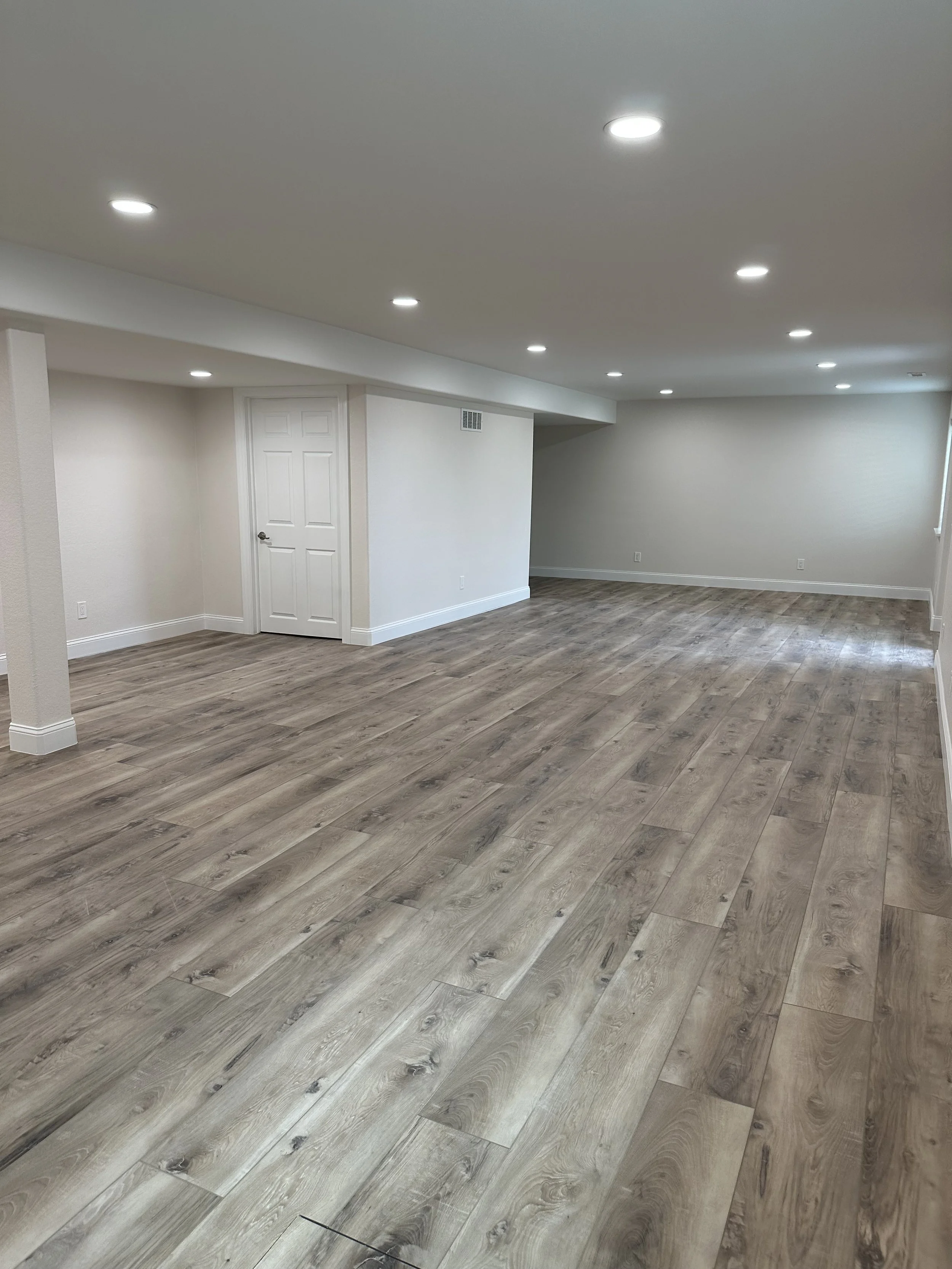 Empty room with wood-look flooring and white walls, with some ceiling recessed lights.