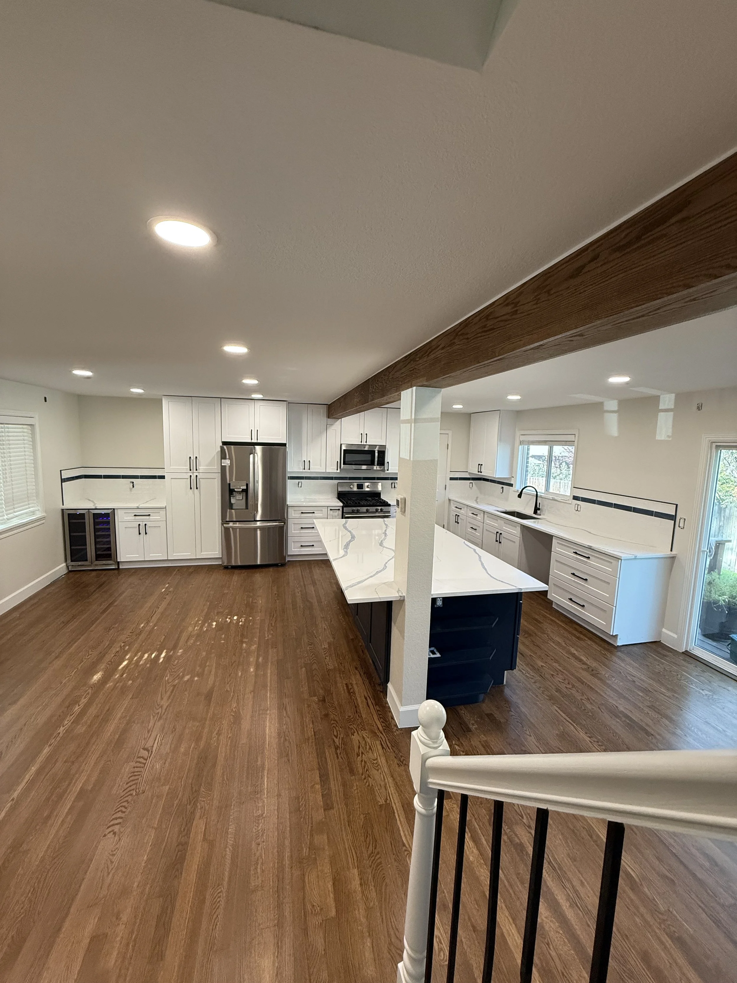 Bright, modern kitchen with white cabinetry, stainless steel appliances, a marble countertop island, and hardwood floors.