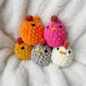 Five colorful crochet plush balls resembling animals with embroidered faces resting on a white fabric background.