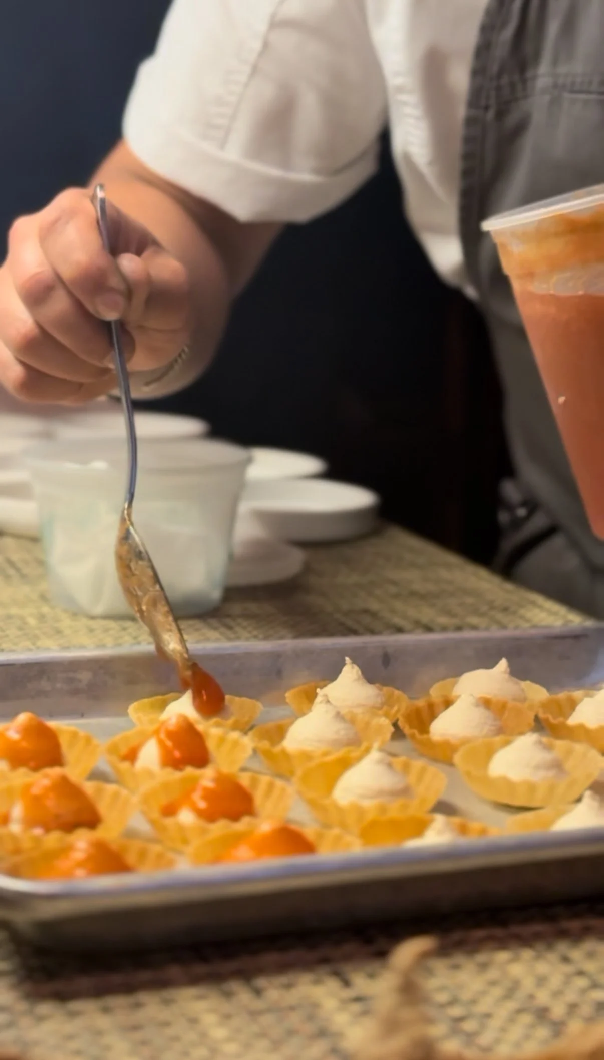 Close-up of someone adding sauce to small appetizer cups filled with creamy topping on a tray.