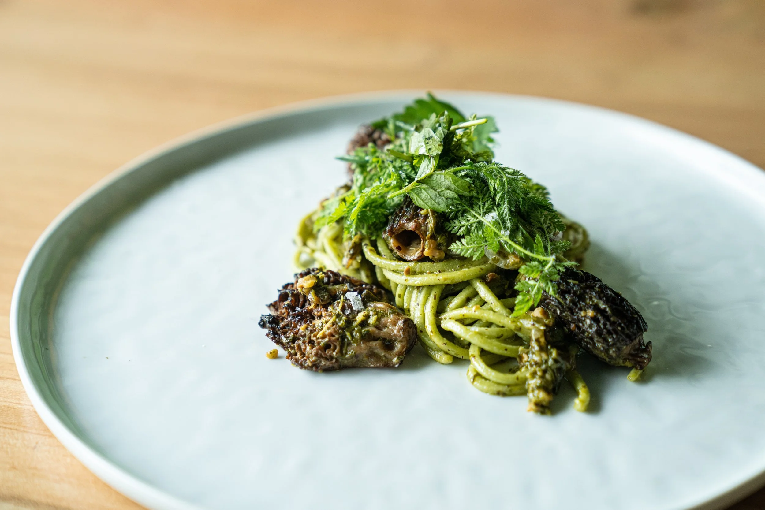 A plate of spaghetti with green sauce, garnished with fresh herbs, served with pieces of meat or vegetables.