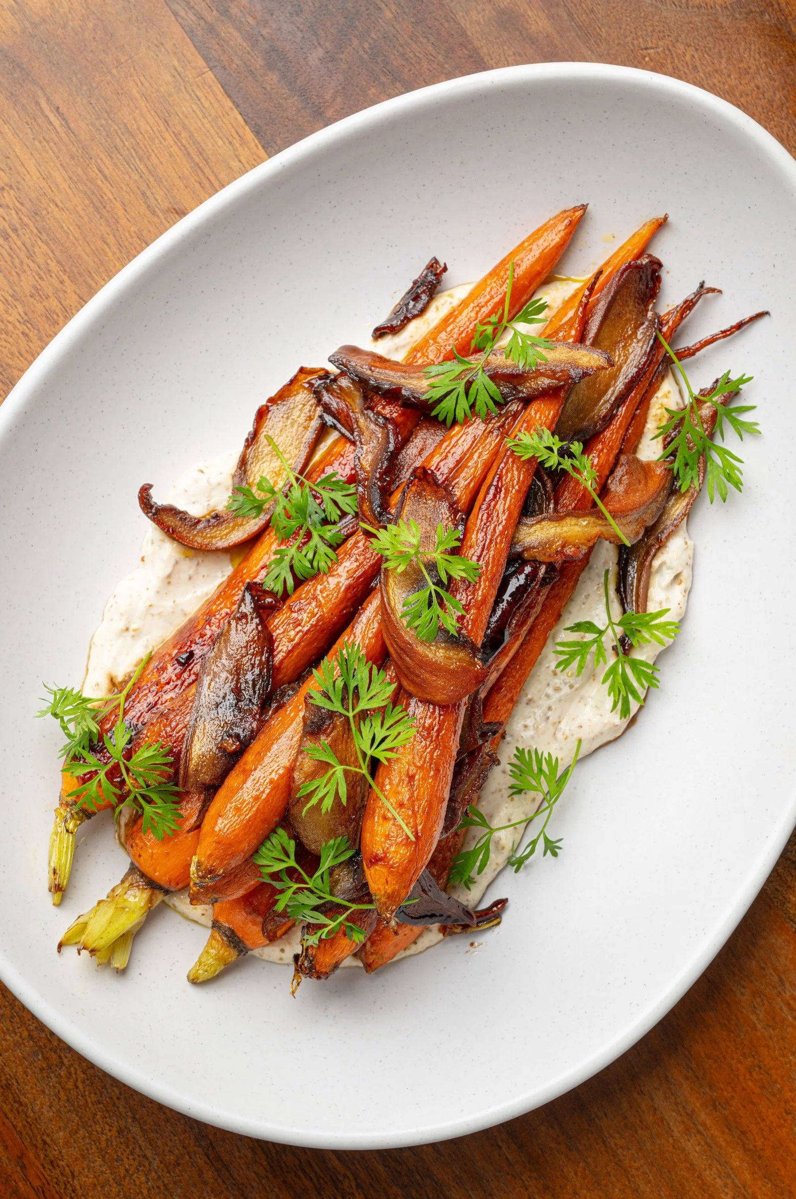 Roasted carrots and mushrooms garnished with fresh herbs served on a white plate.