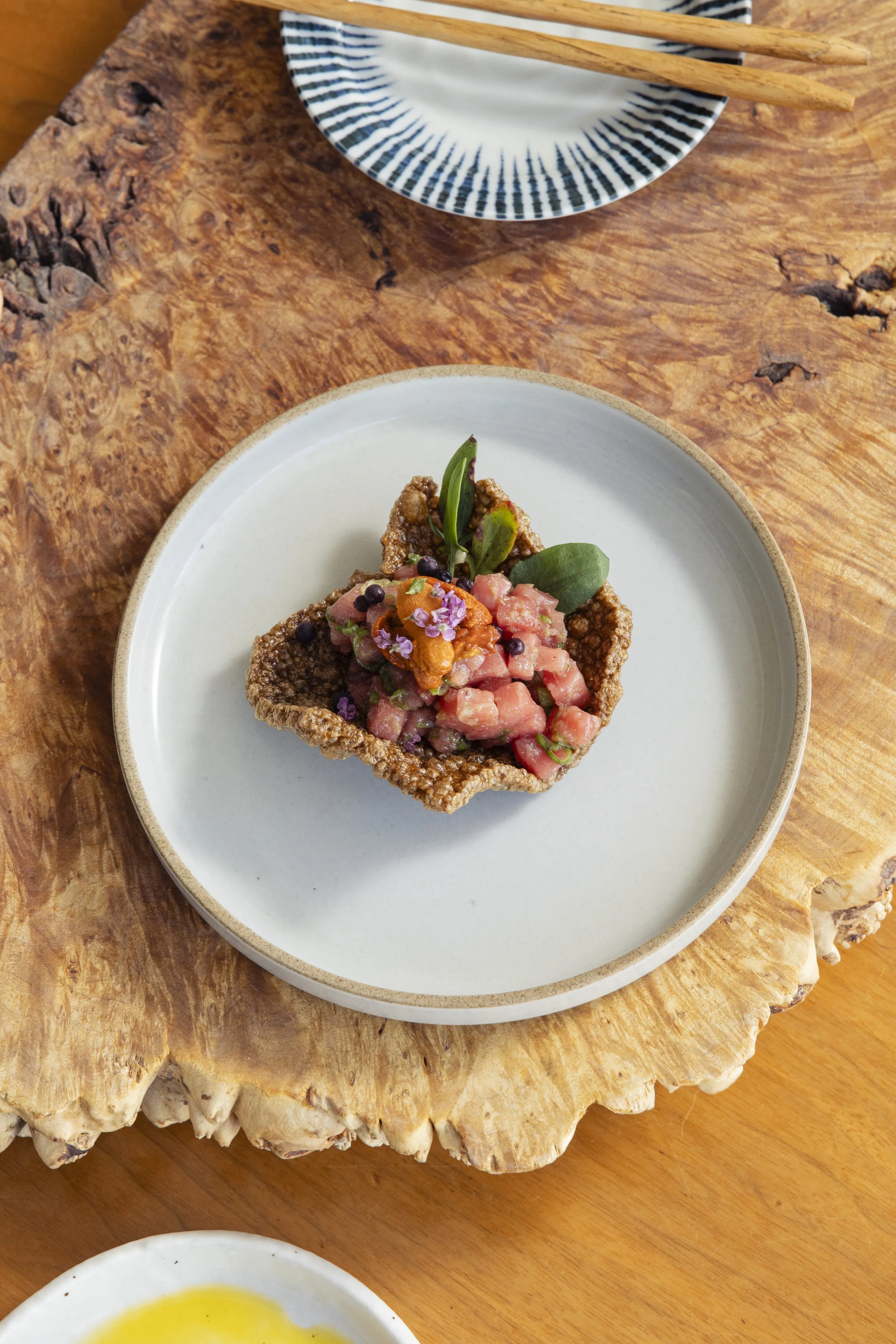 A serving of chopped raw fish tartare garnished with herbs, edible flowers, and peppercorns, on a white plate.