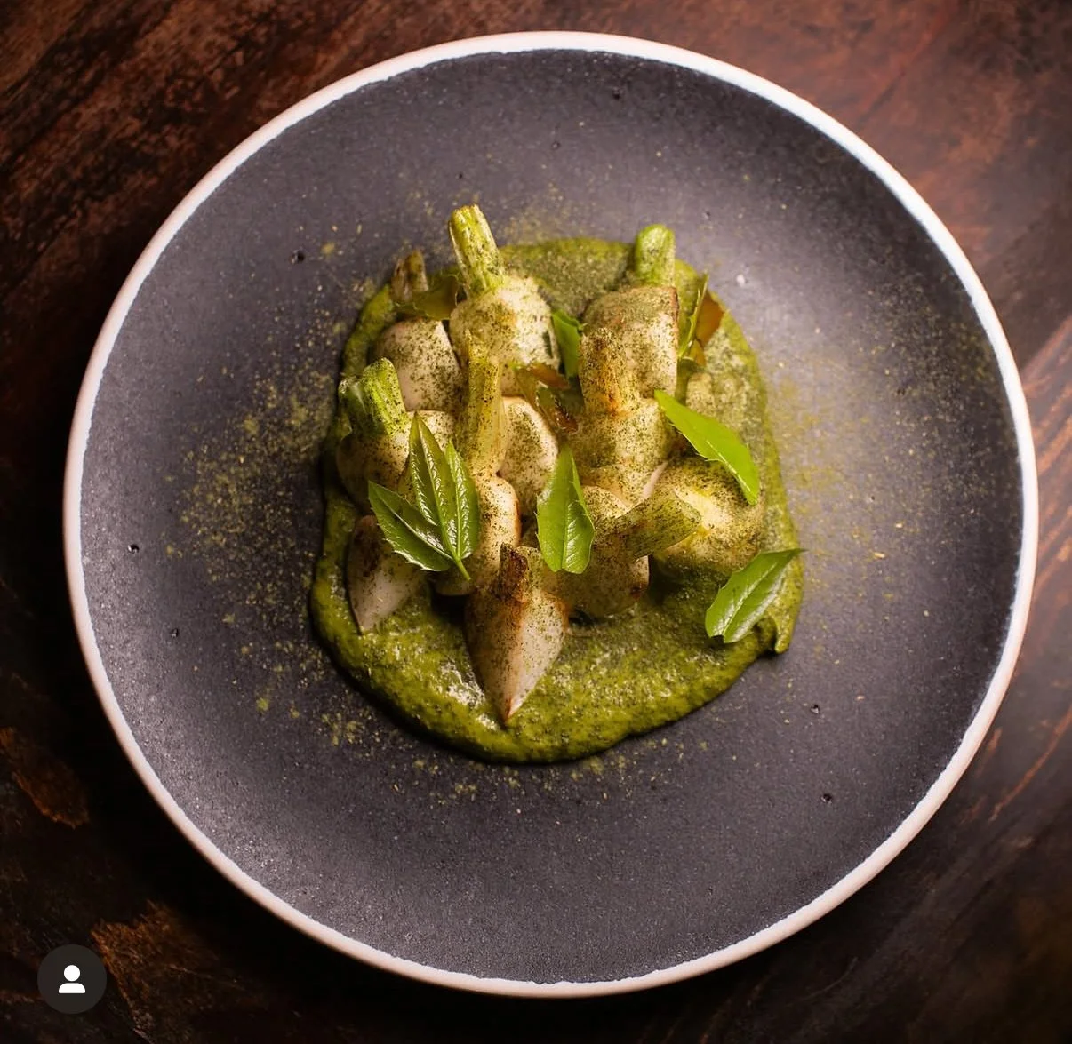 A bowl of green sauce with layered vegetables and fresh green leaves.